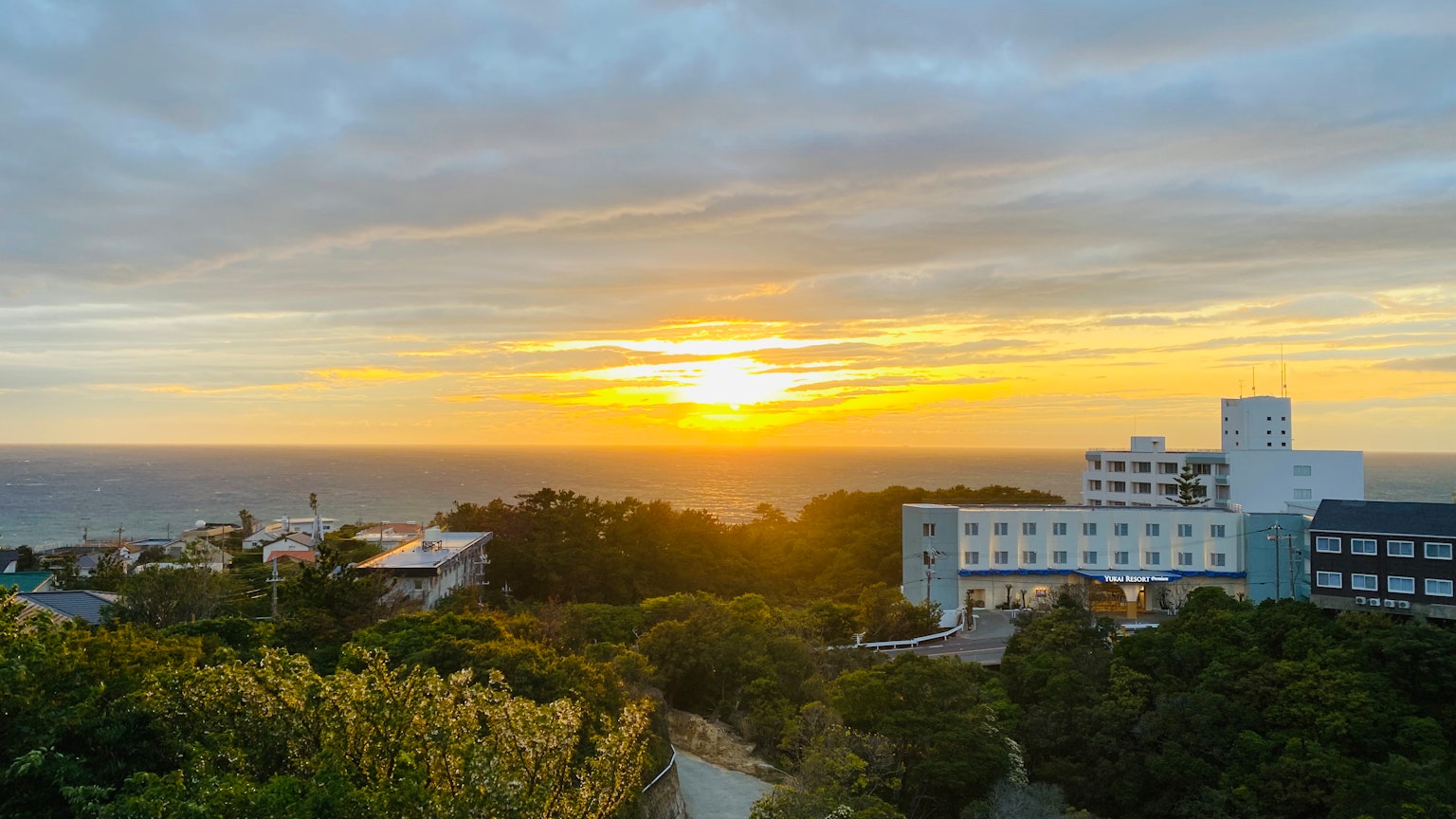 Vista panoramica dell'oceano al tramonto con nuvole e vegetazione vicino agli edifici