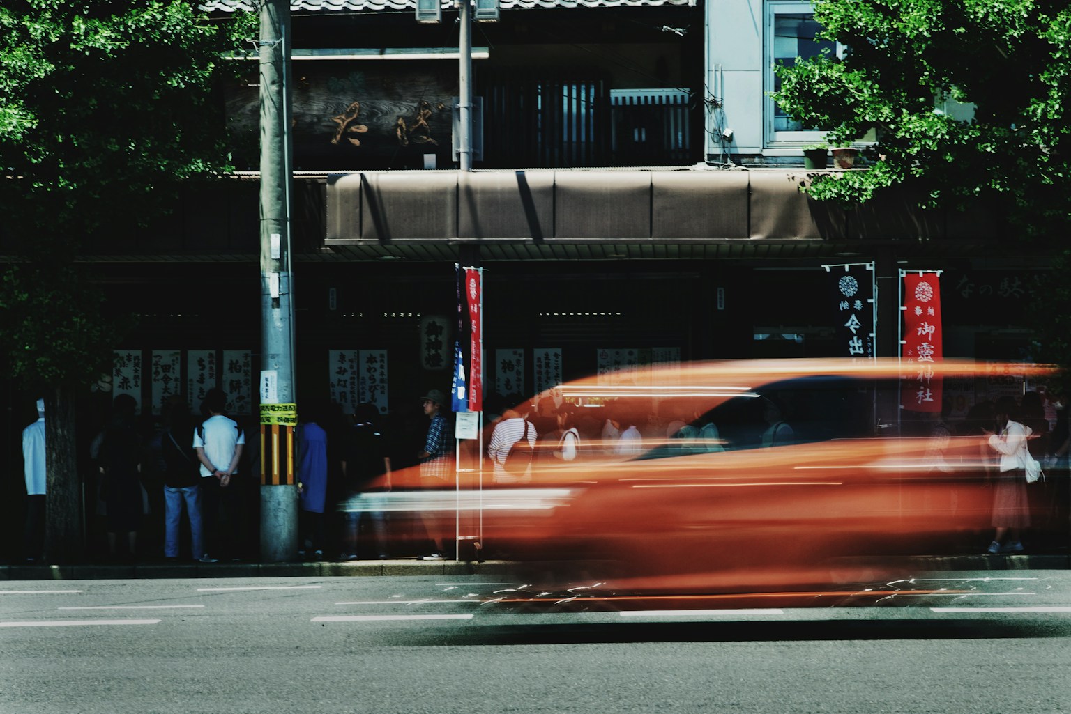 A blurred orange car speeding past an old building with people in the background