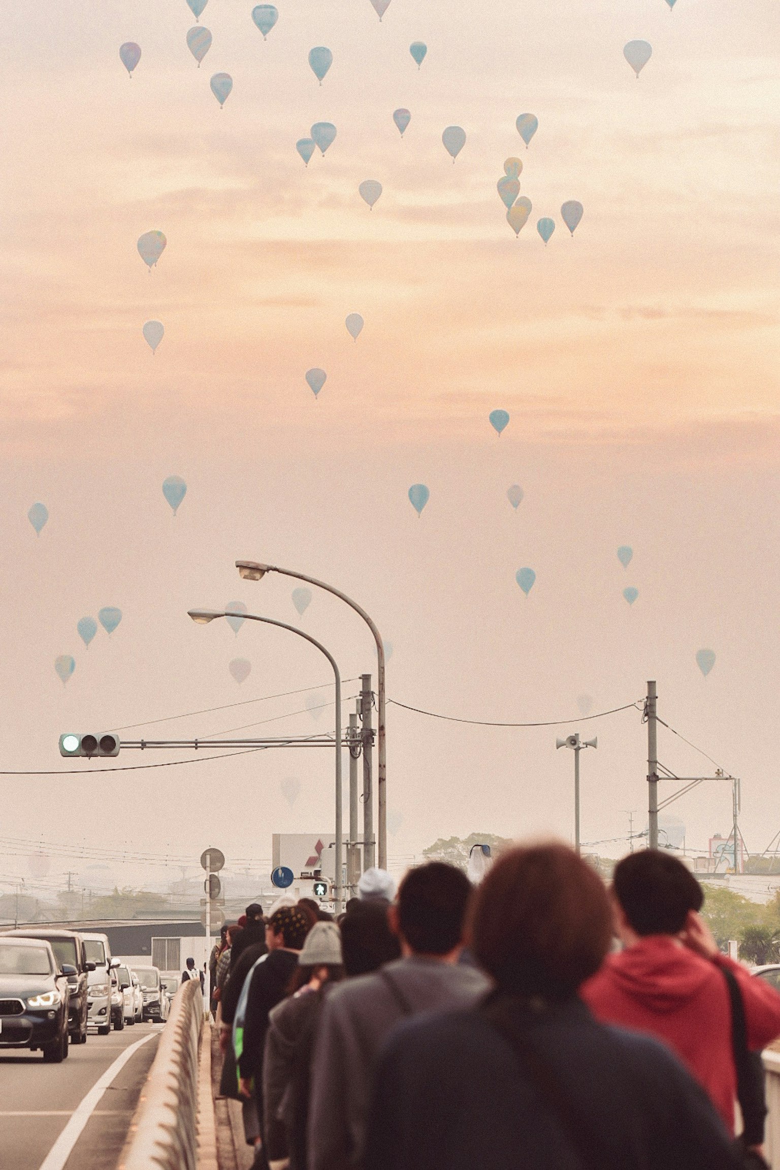 People walking along a road looking up at balloons floating in the evening sky