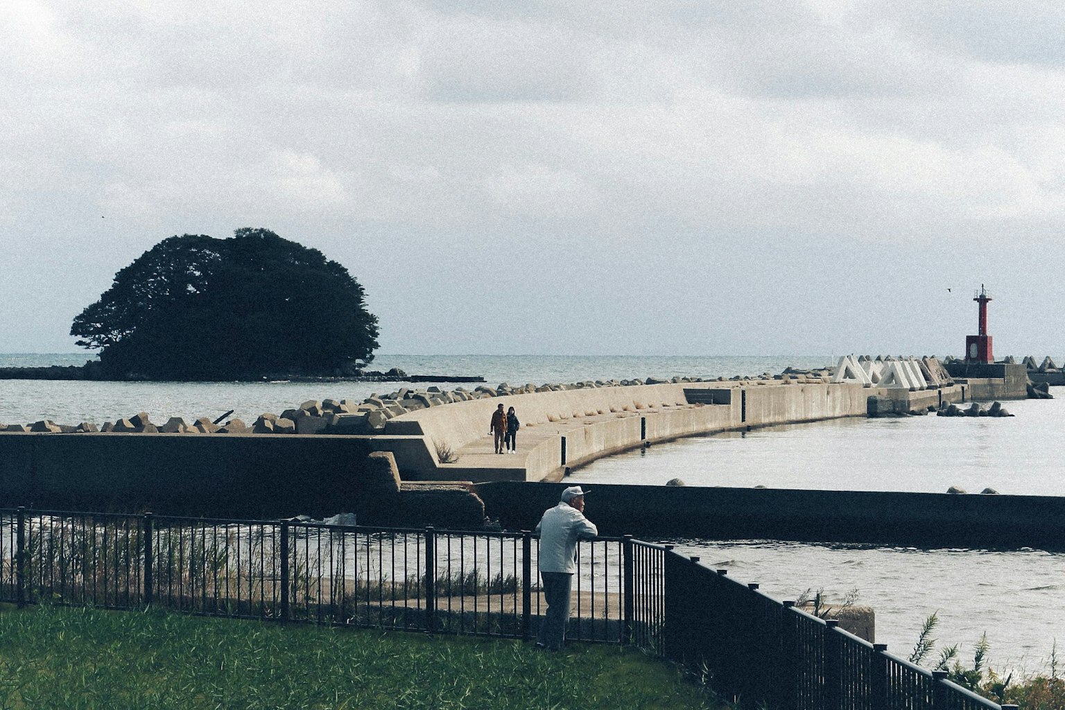 Küstenansicht mit einem Wellenbrecher und einem Leuchtturm im Hintergrund