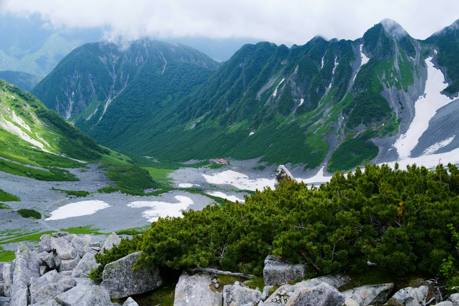 Vue pittoresque de montagnes vertes et de vallées enneigées avec des buissons entre les rochers