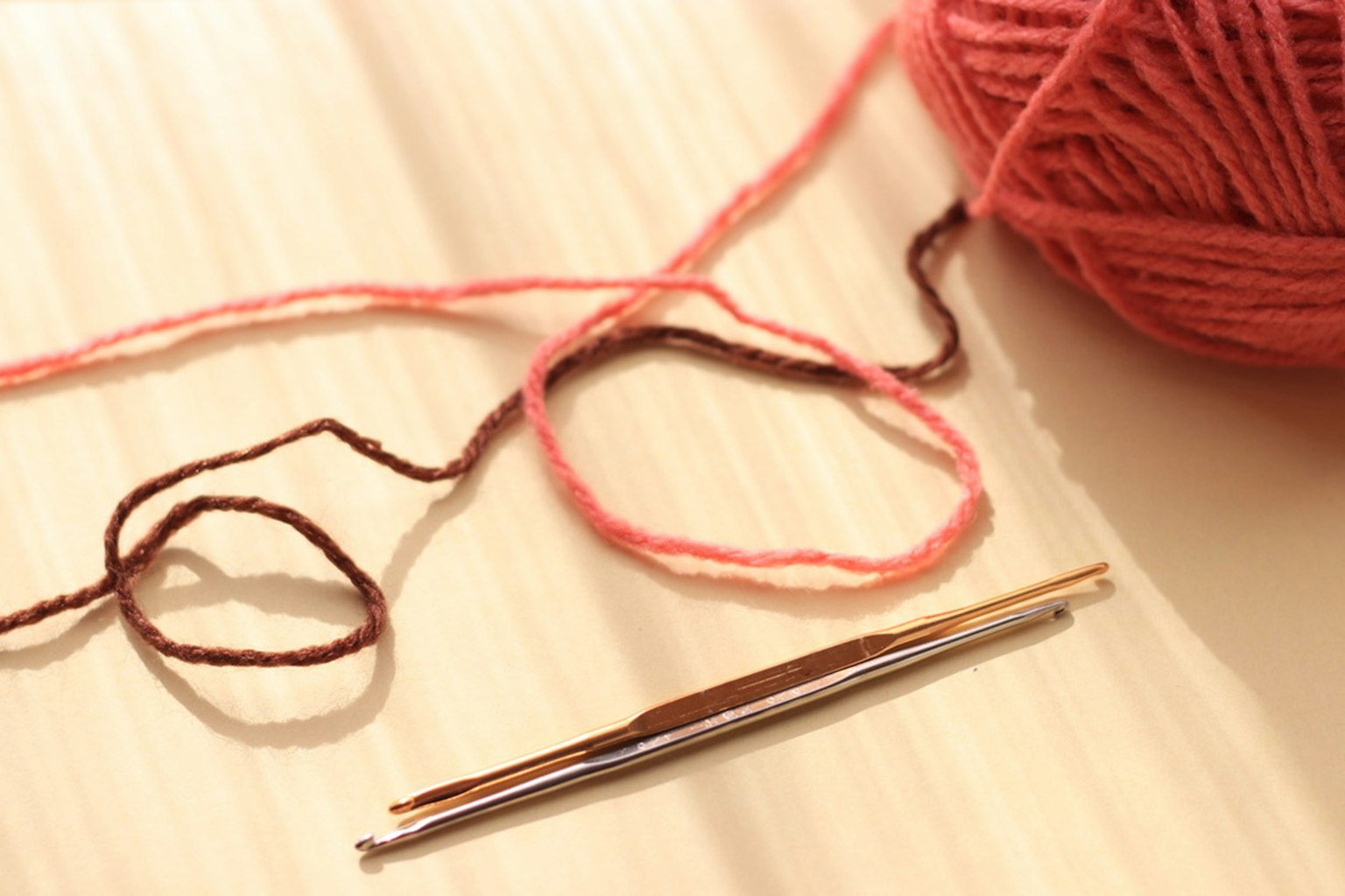 Bild von rosa Garn und einer Häkelnadel Das Garn ist weich und hat helle Farben Die Häkelnadel ist metallisch und glänzend