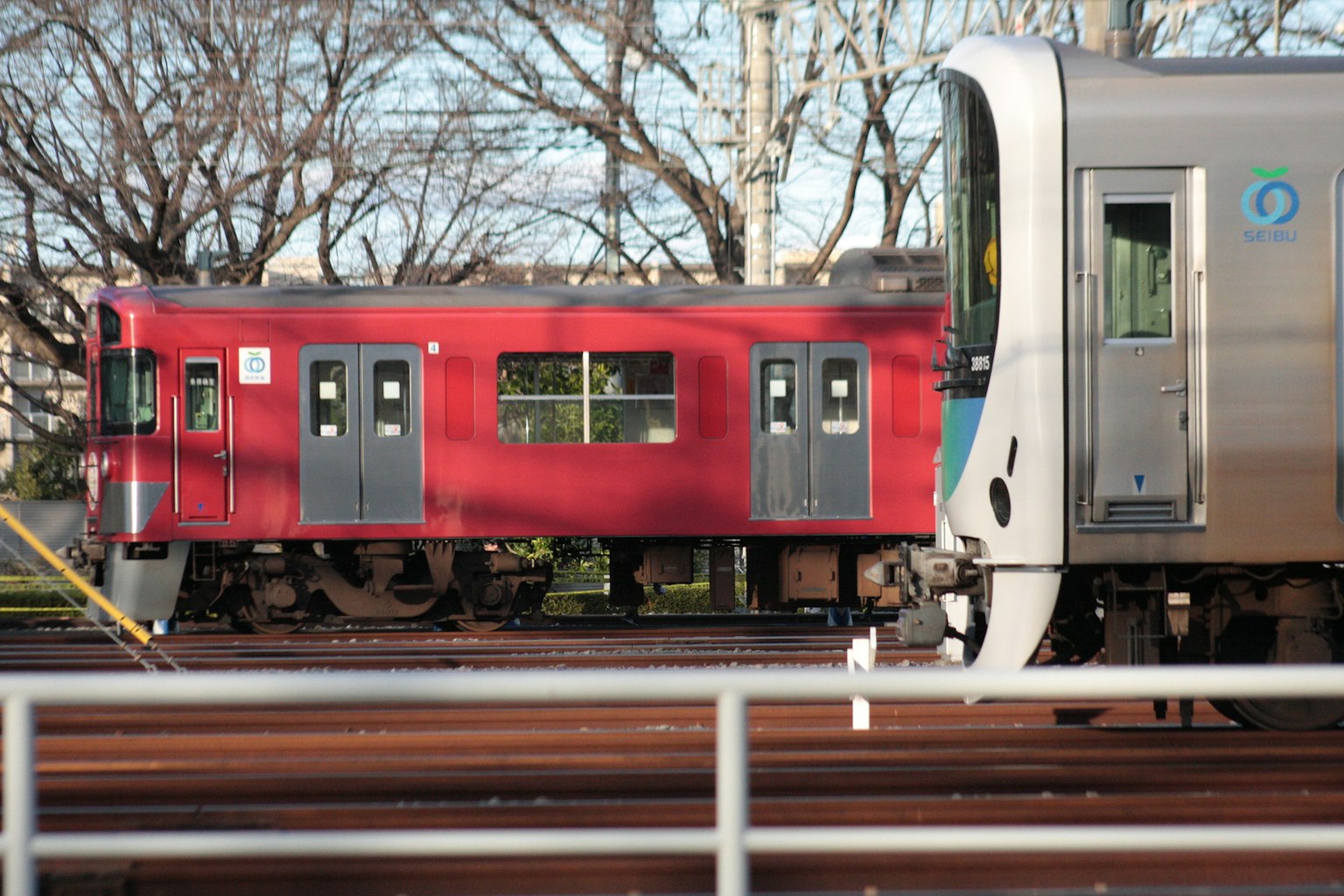 Red train and silver train side by side in a railway setting