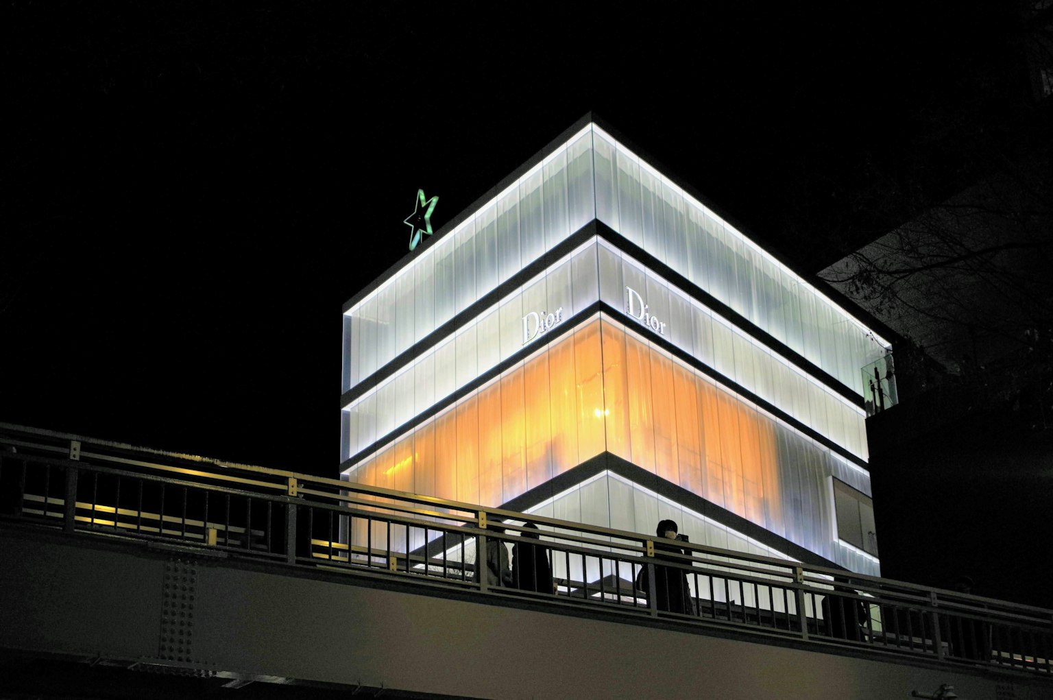 Modern building illuminated at night with glowing exterior and silhouettes of people