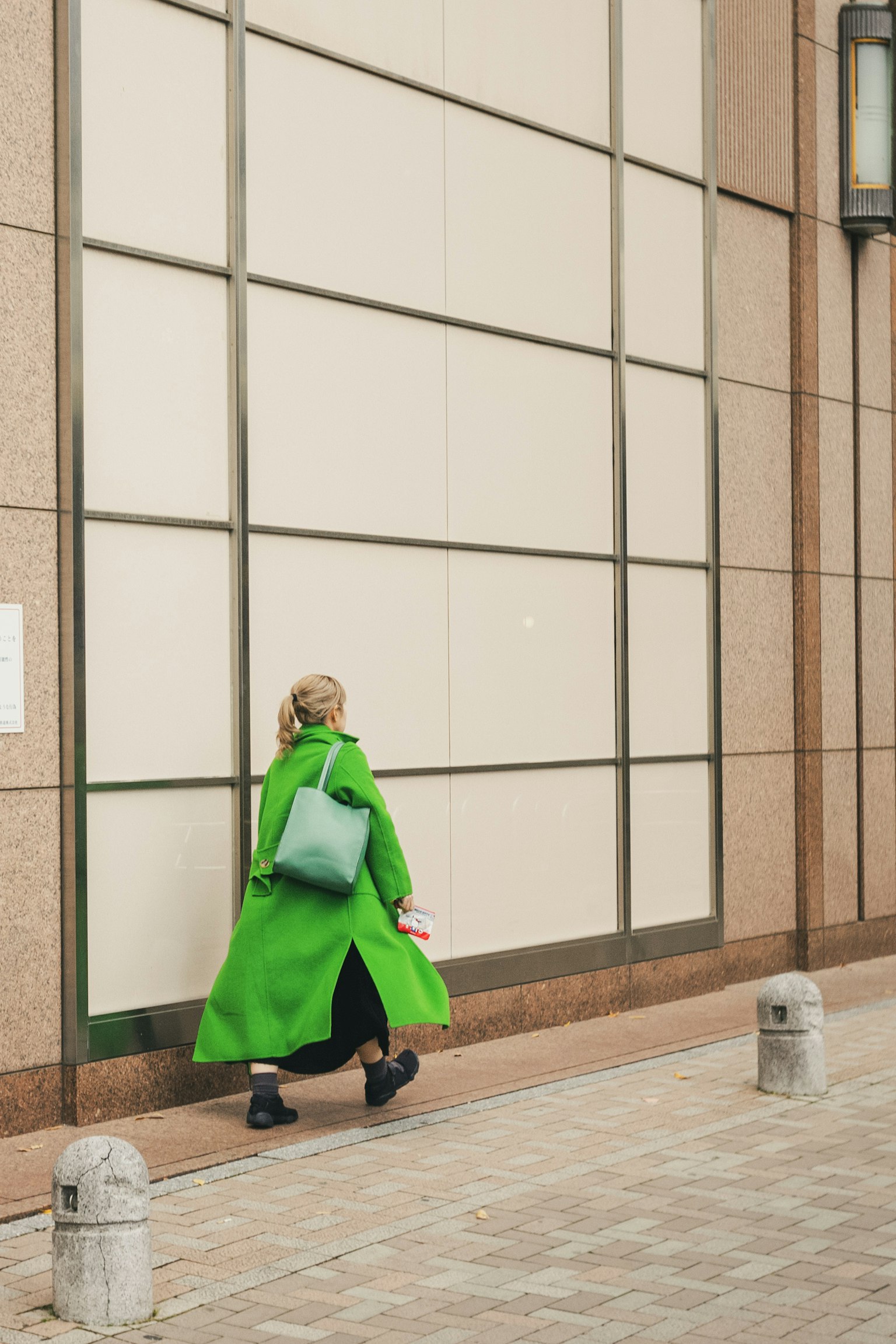 A woman in a green coat walking along a building wall