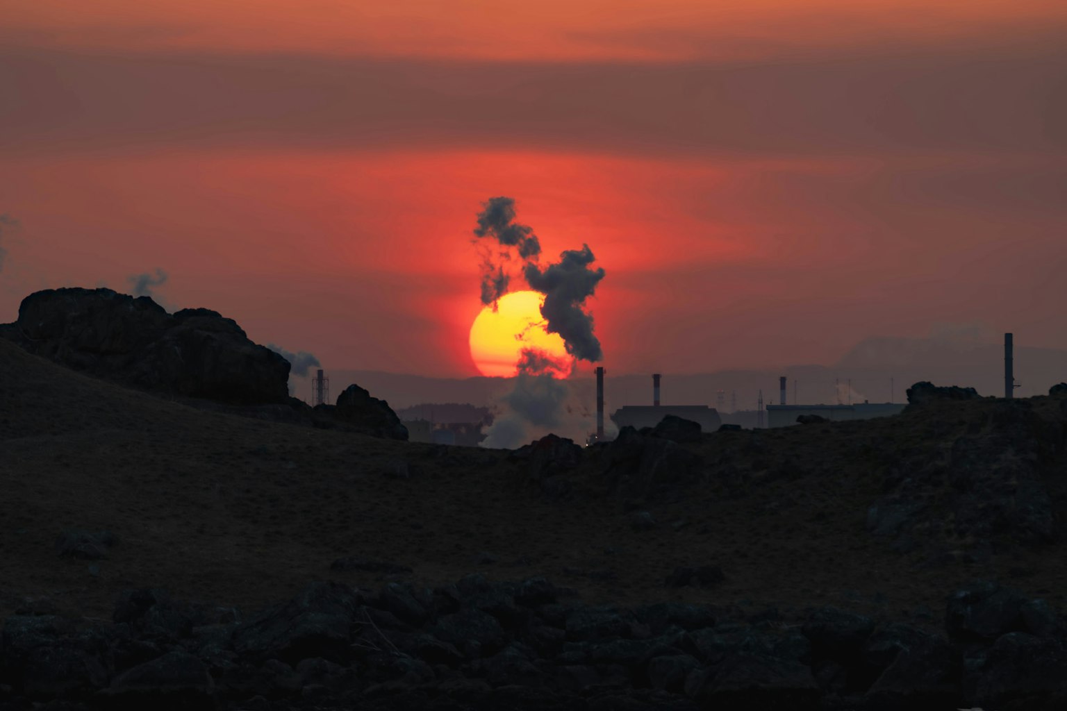 Silueta de una fábrica emitiendo humo contra un atardecer