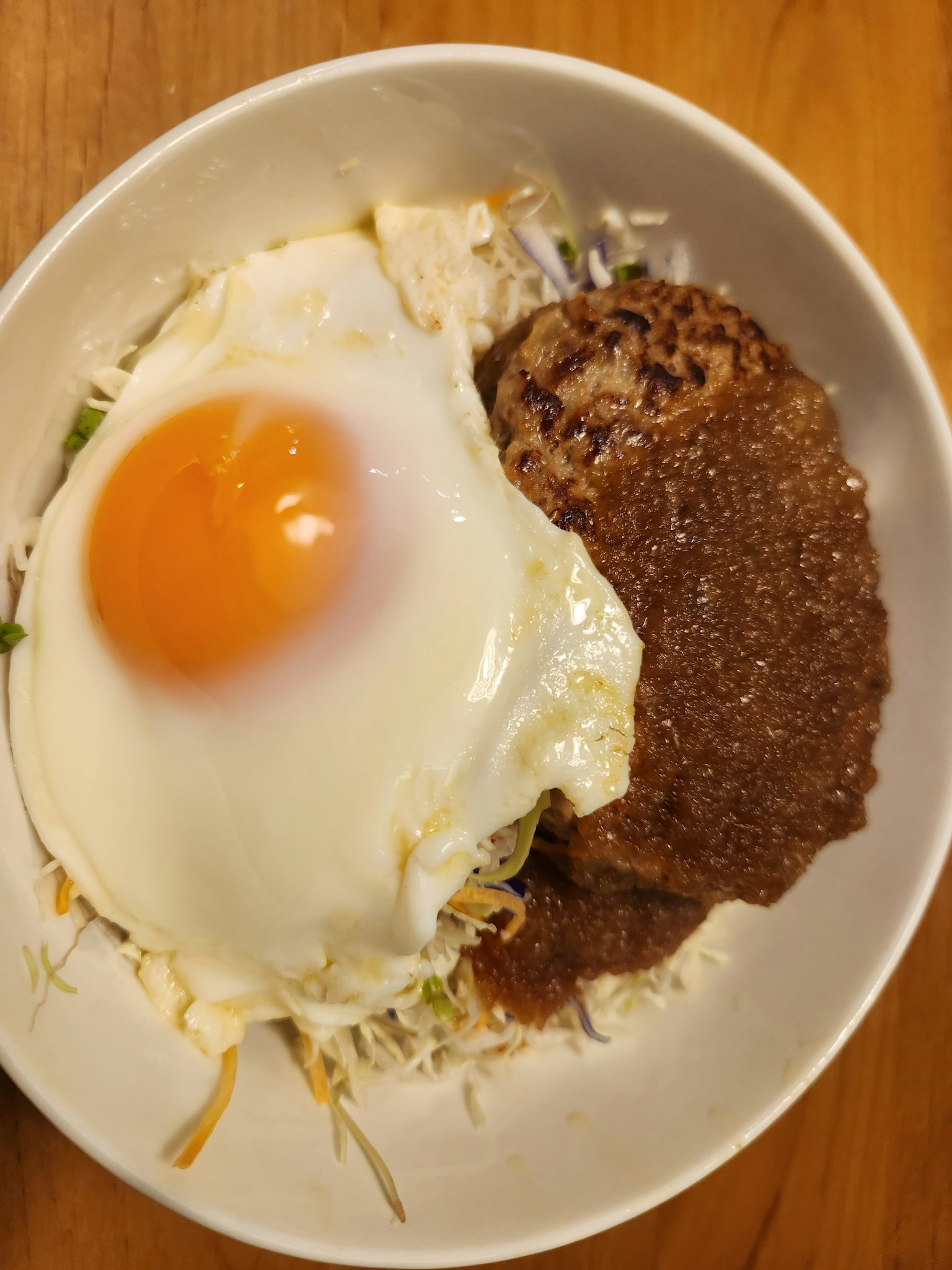 Ein weißer Teller mit Reis, belegt mit einem Spiegelei und einem mit Sauce übergossenem Hamburgersteak