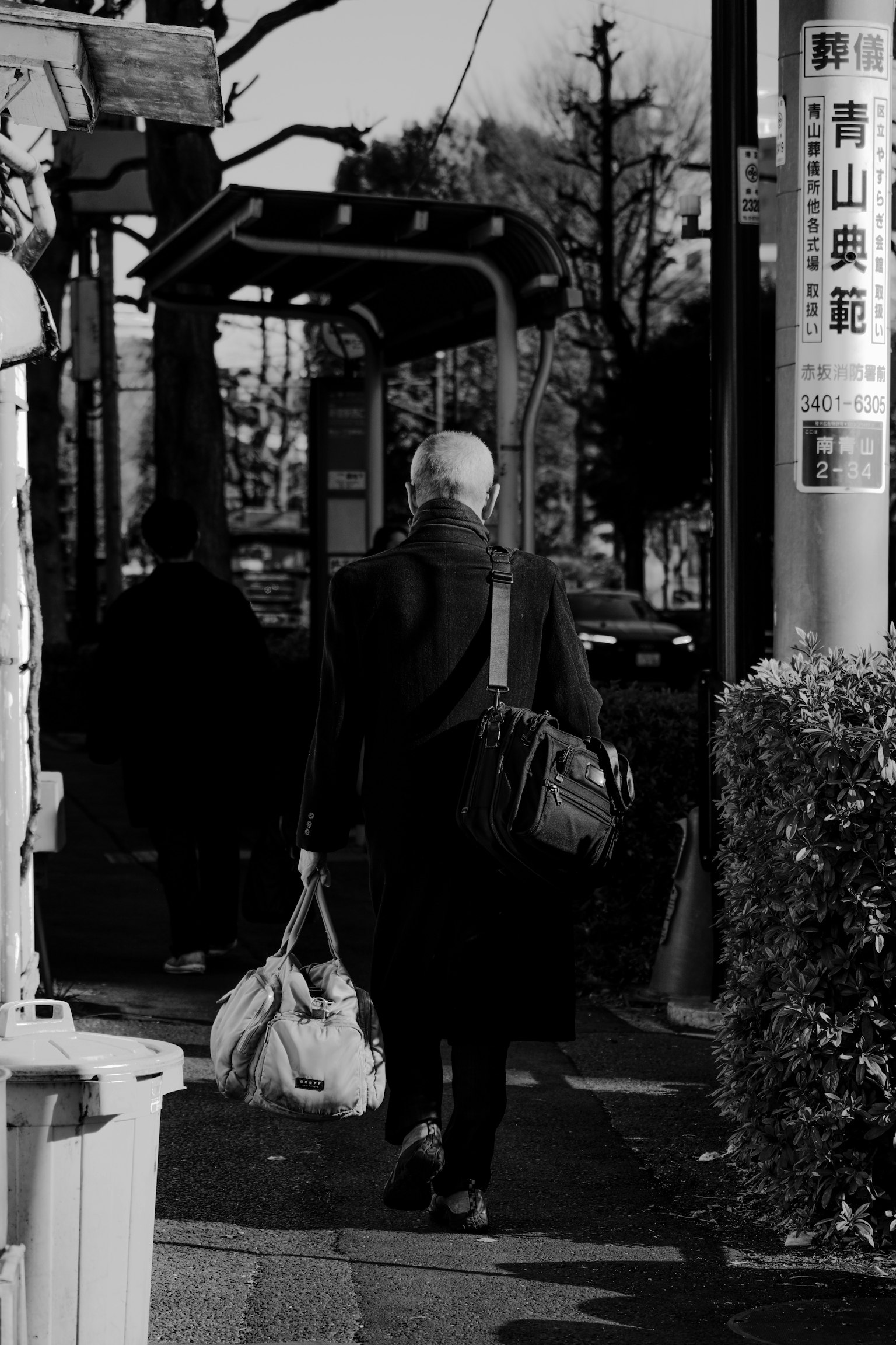 Photo en noir et blanc d'un homme avec un sac marchant vers un arrêt de bus