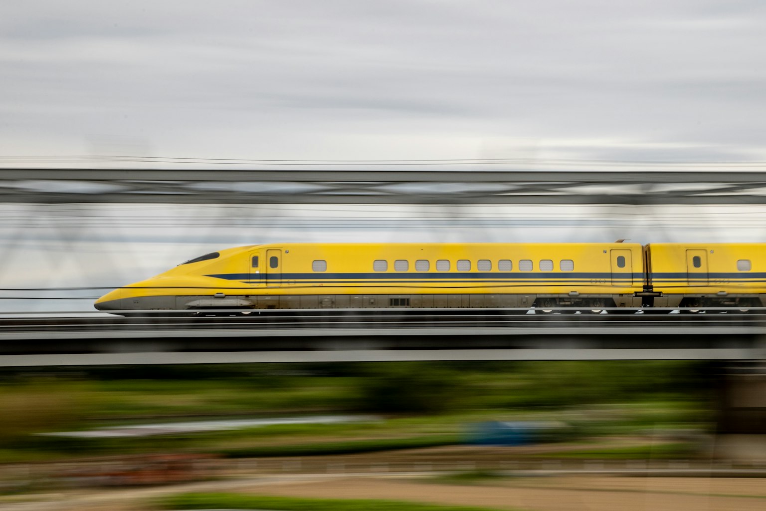 Yellow Shinkansen train speeding past on a bridge