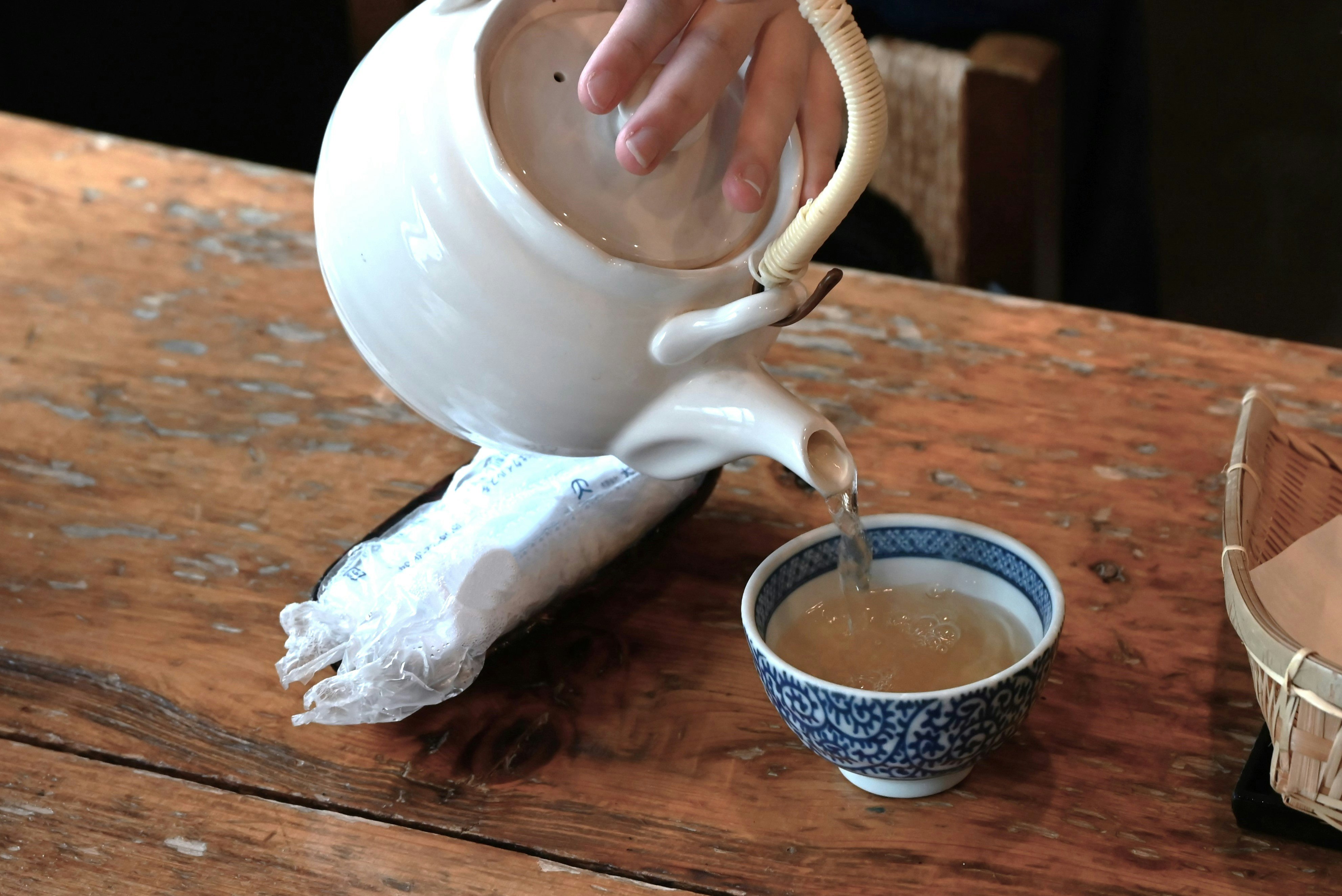 木桌上白色茶壺向小茶杯倒熱茶