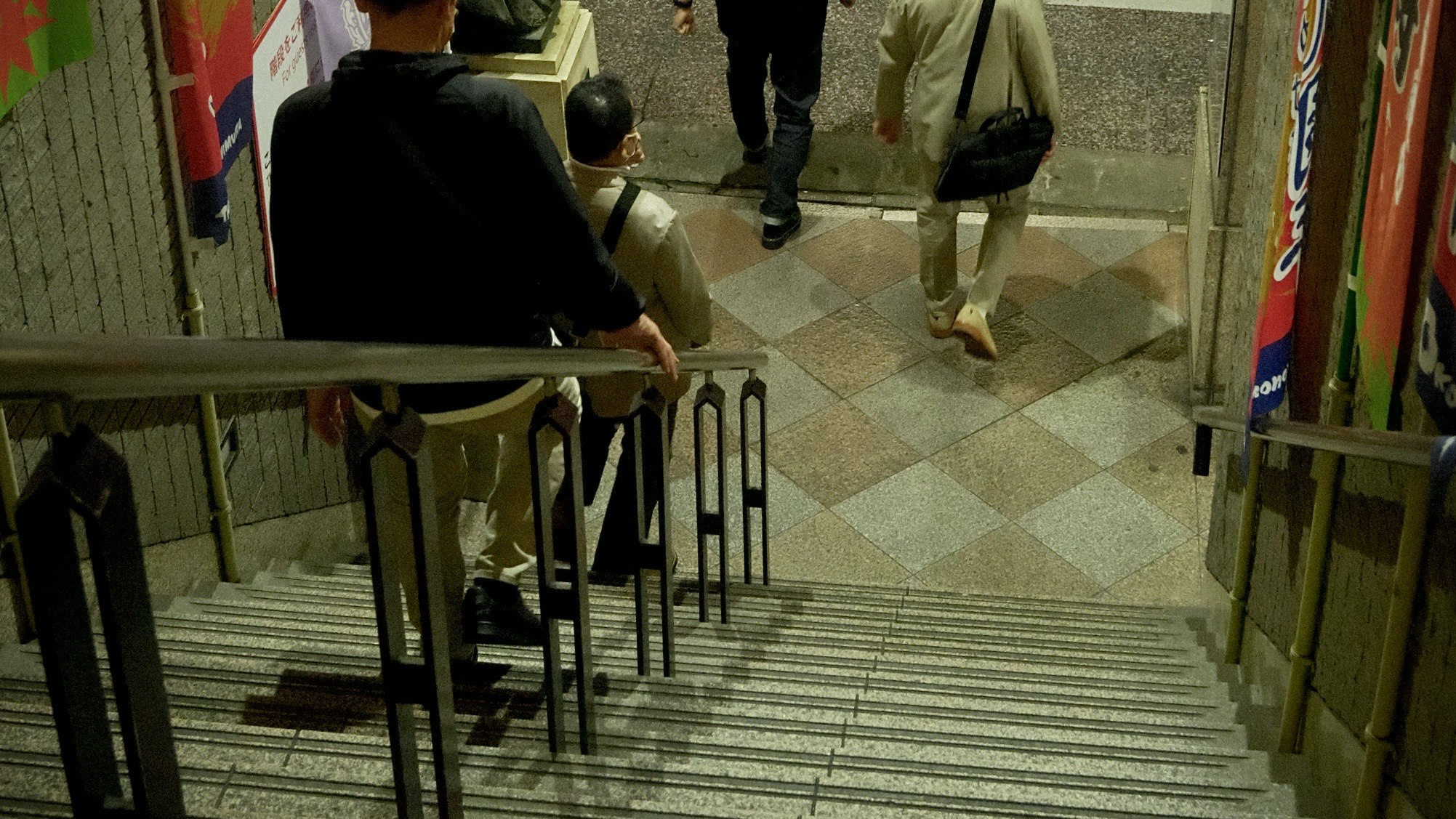 Menschen, die Treppen hinuntergehen, mit bunten Postern an den umliegenden Wänden