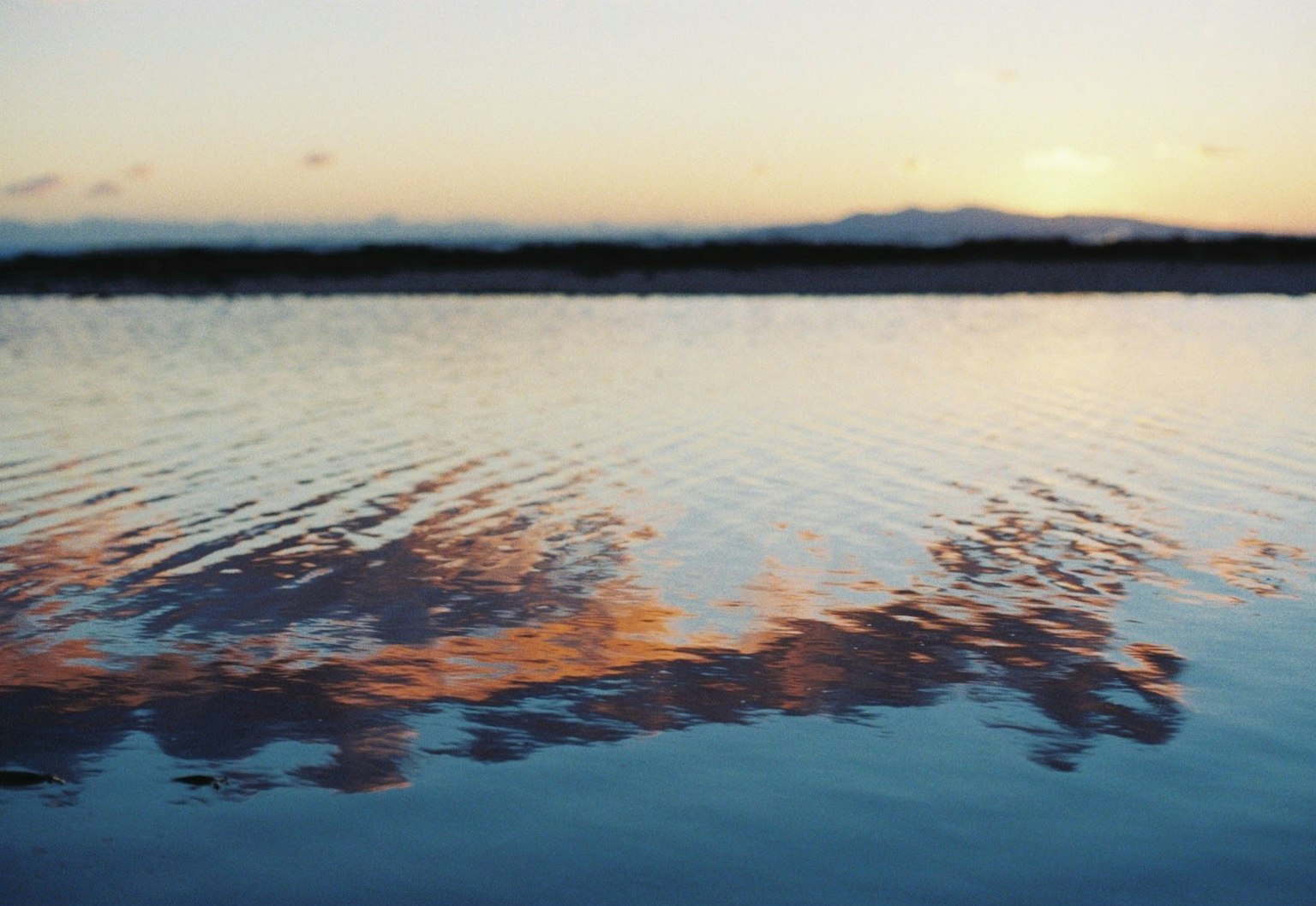 Superficie de agua serena reflejando el atardecer y las nubes
