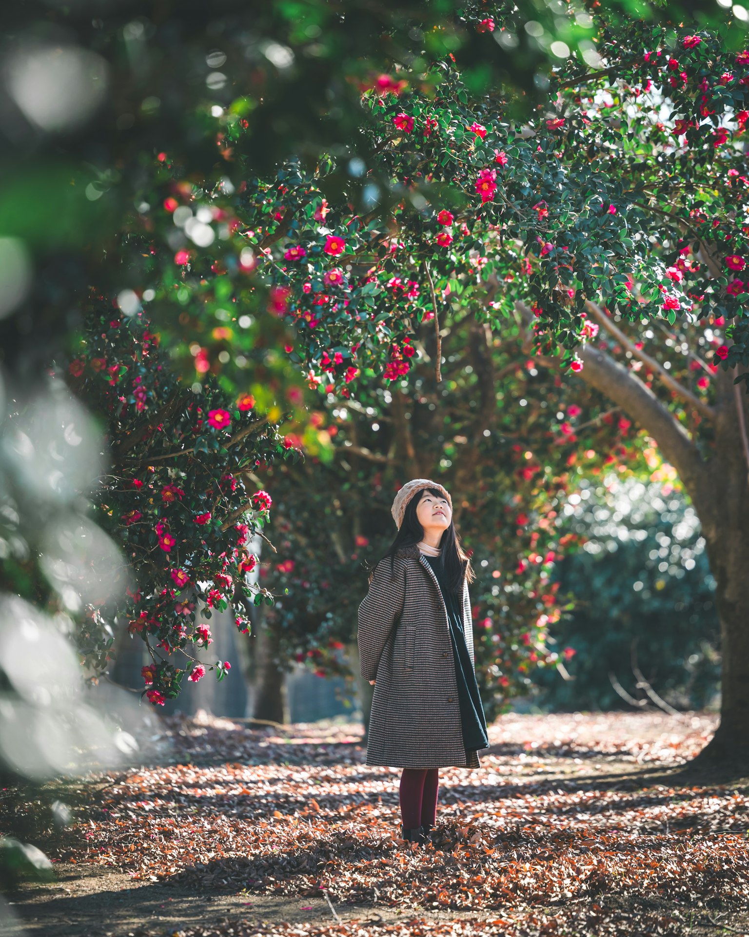 A girl in a coat standing under trees with colorful flowers