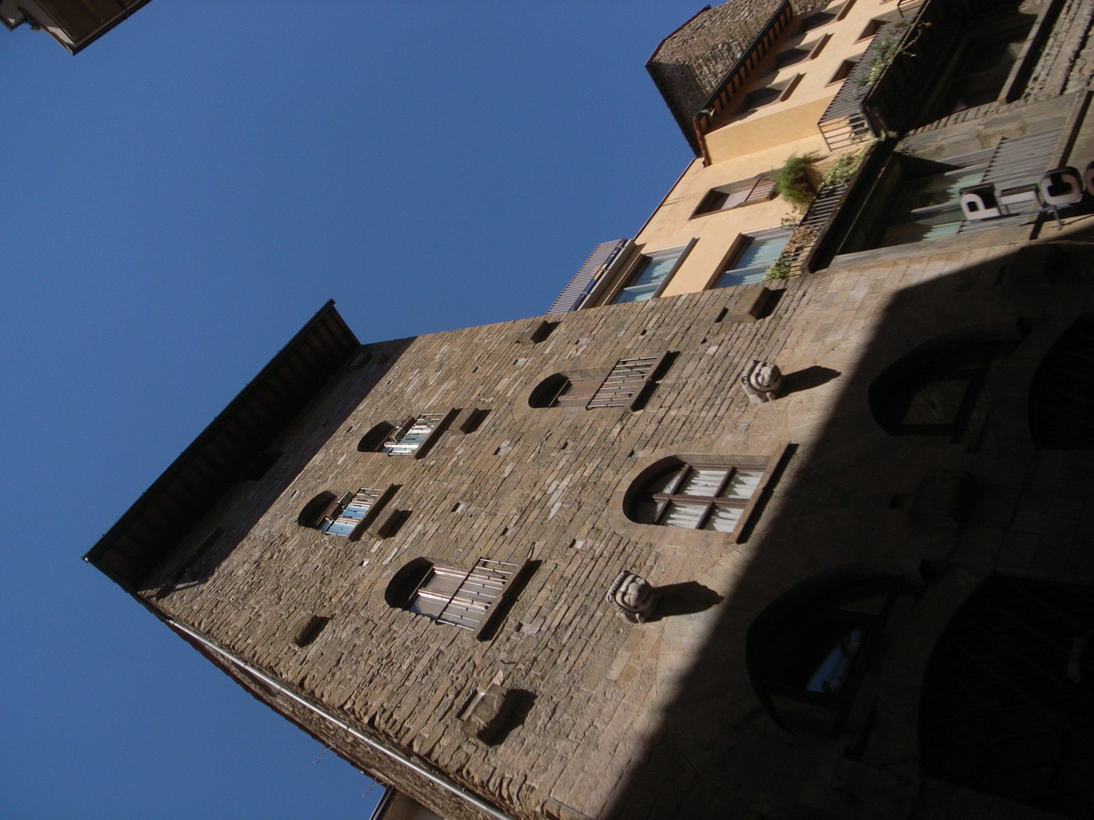 Edificio in pietra con più finestre e ombre contro un cielo blu