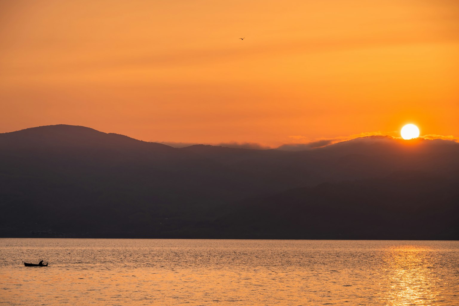 Sunset over a lake with silhouettes of mountains