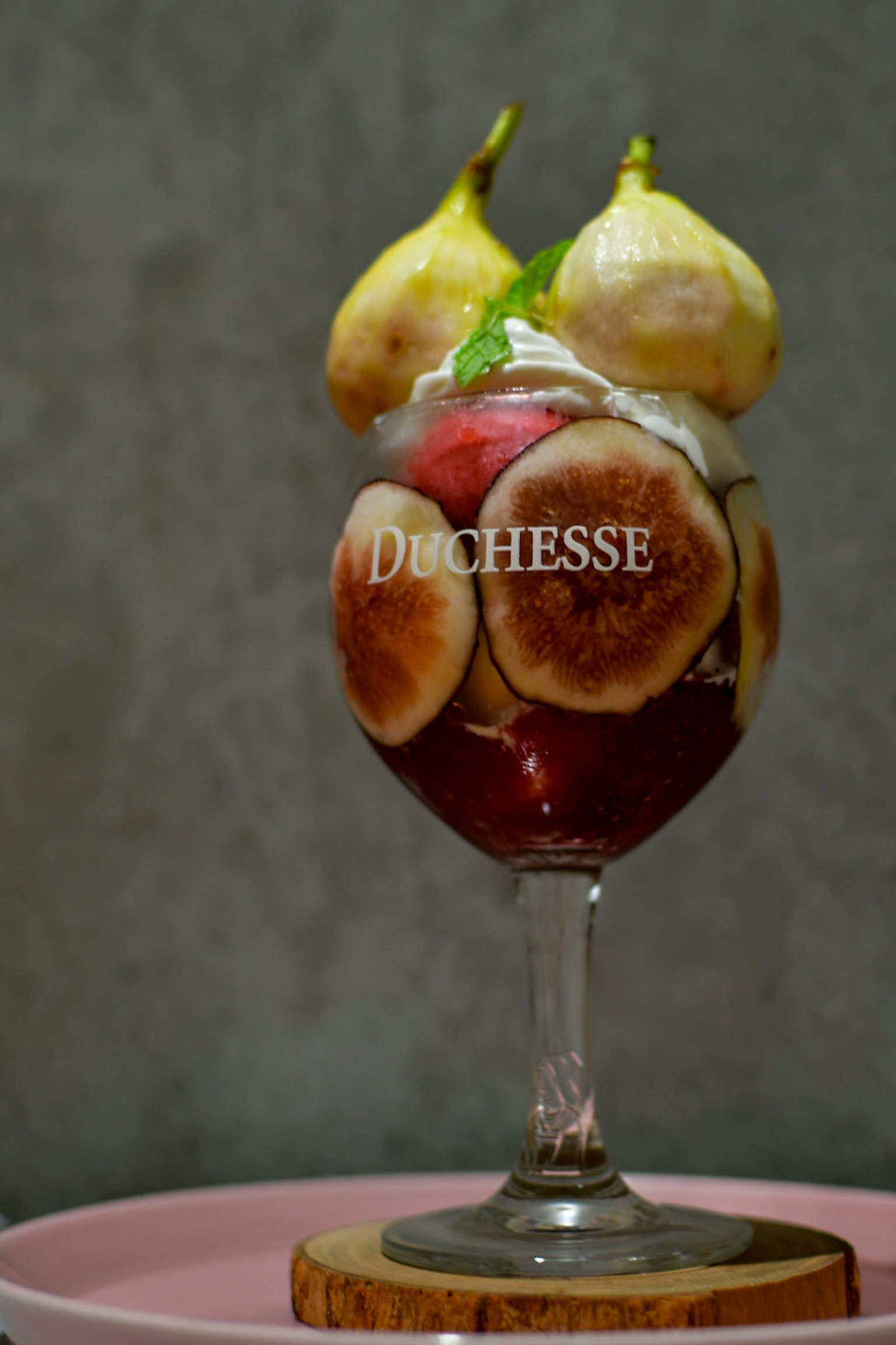 A dessert glass filled with a fruit sundae topped with two pears and figs with whipped cream