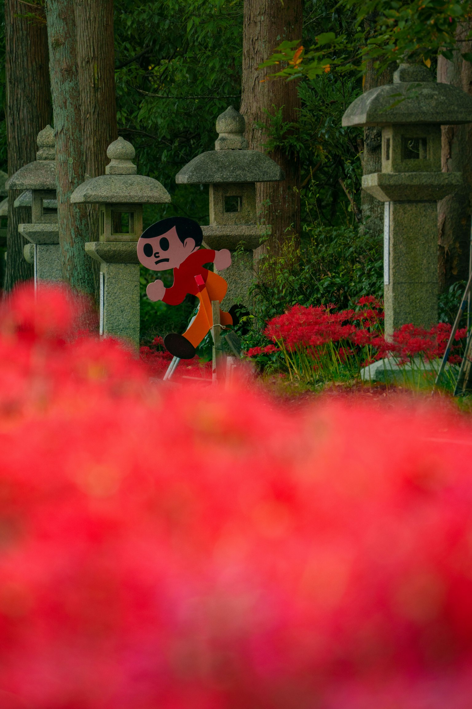 Anime character standing in front of red flowers and stone lanterns