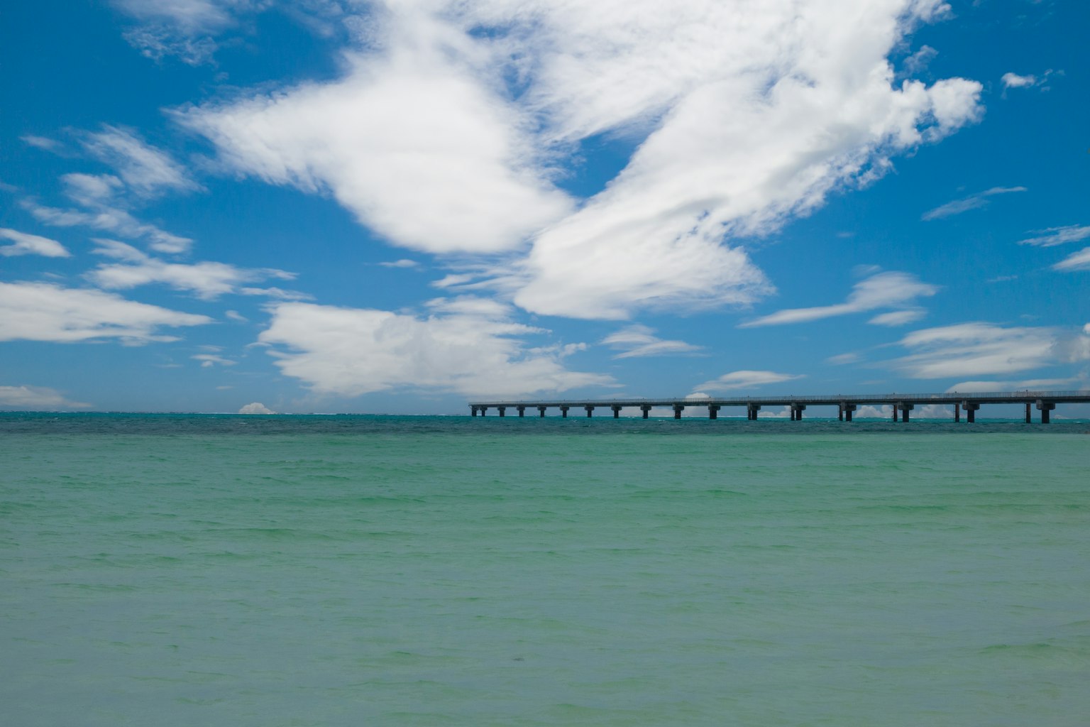 Mar tranquilo bajo un cielo azul con nubes blancas y un muelle