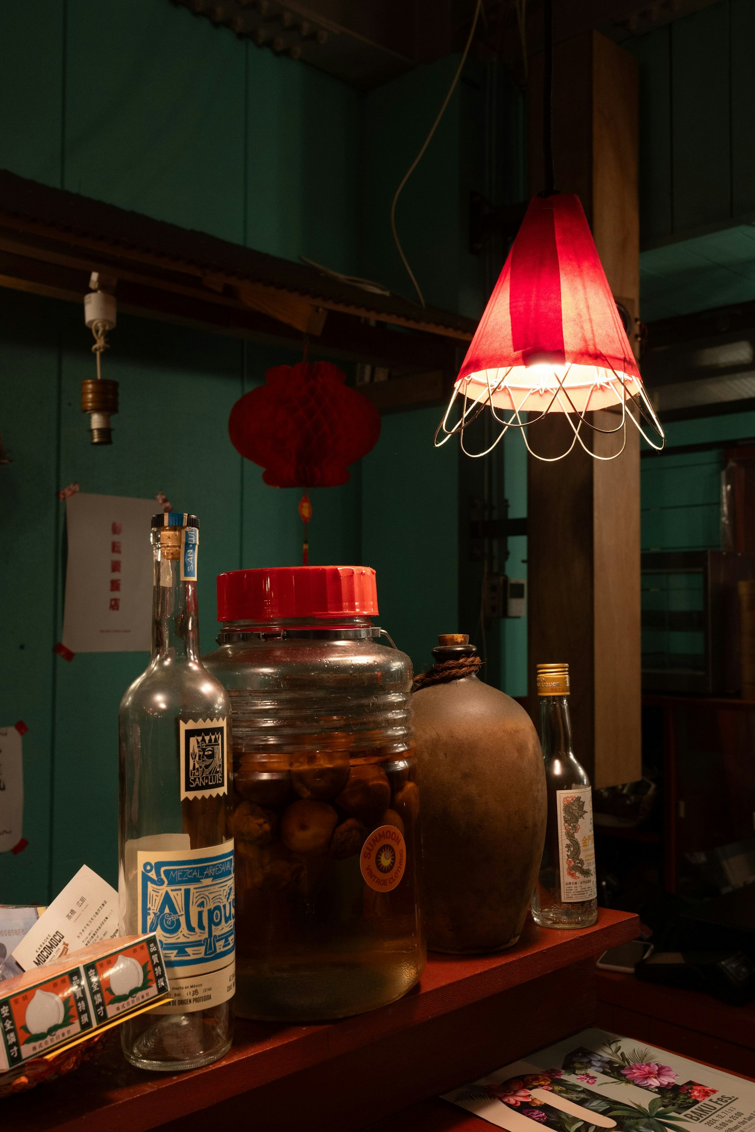 Comptoir avec diverses bouteilles et un abat-jour rouge illuminant la scène