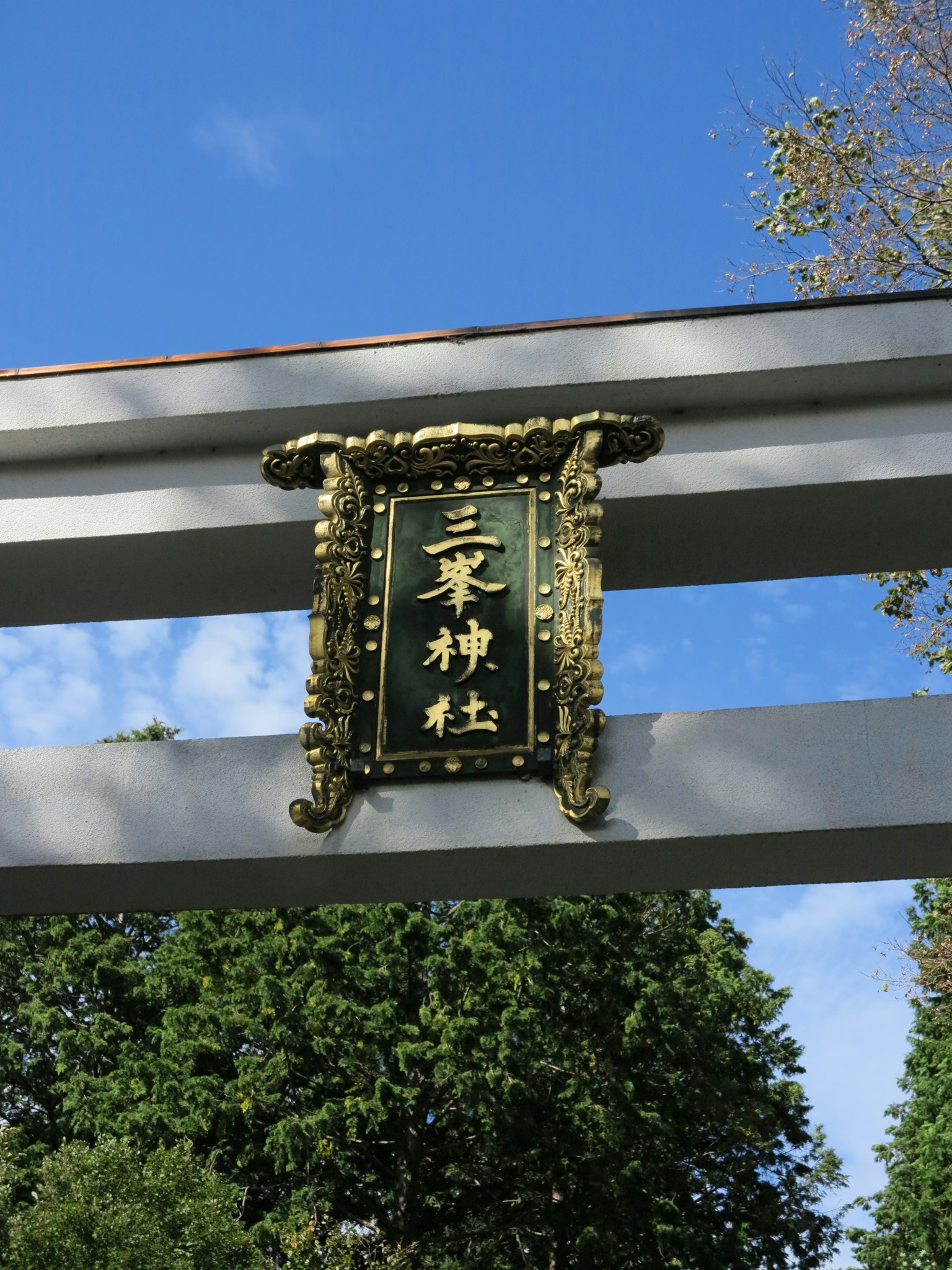 Traditionelles Tor mit goldenen Buchstaben vor grünen Bäumen