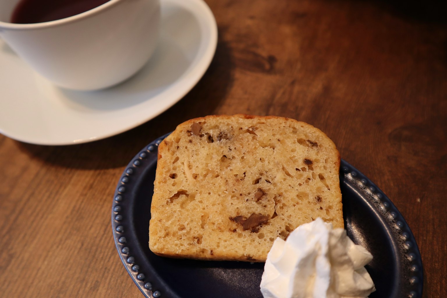 A slice of cake with whipped cream next to a cup of coffee on a wooden table