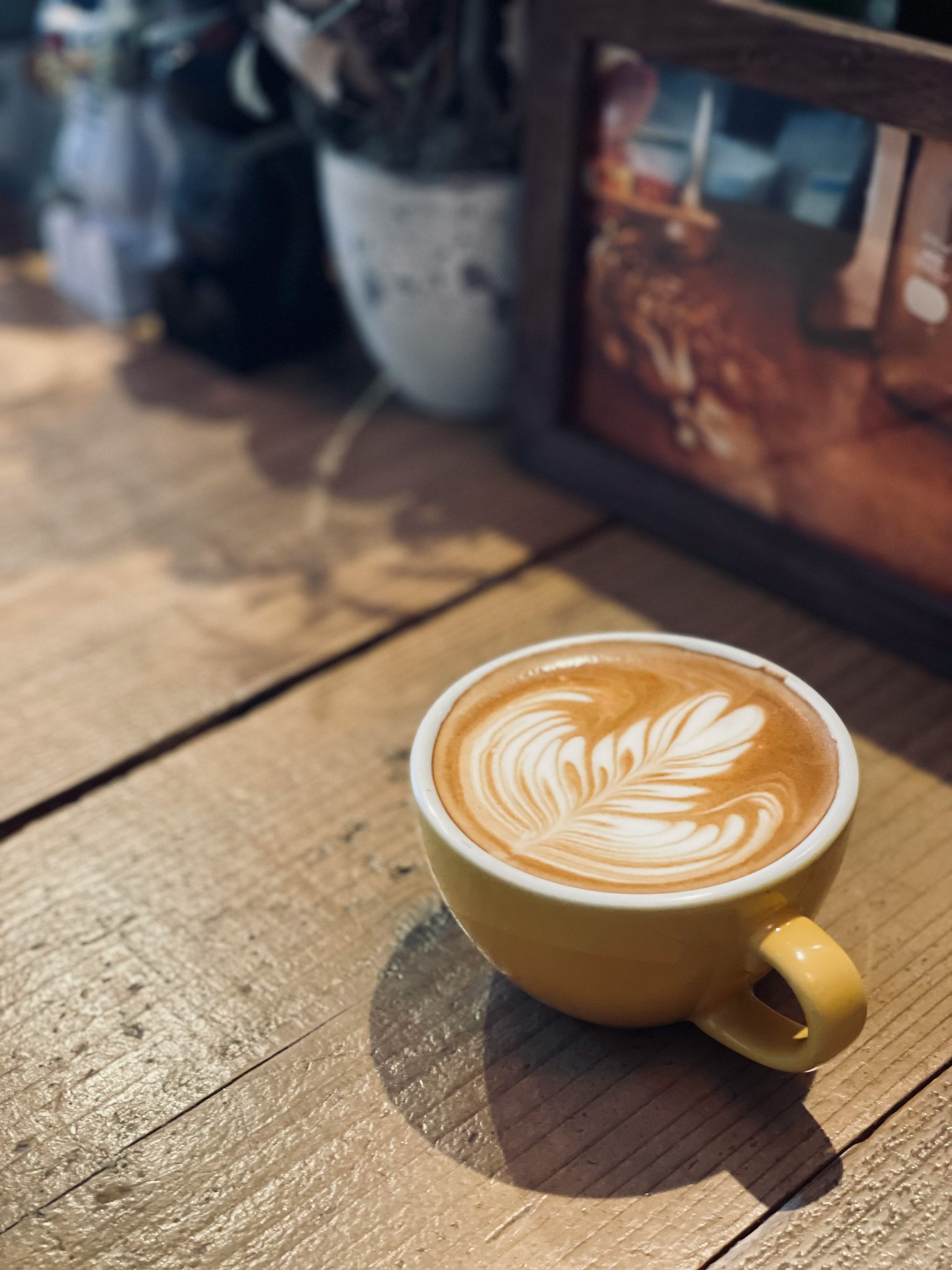 กาแฟลาเต้พร้อมศิลปะลาเต้ในถ้วยสีเหลืองบนโต๊ะไม้