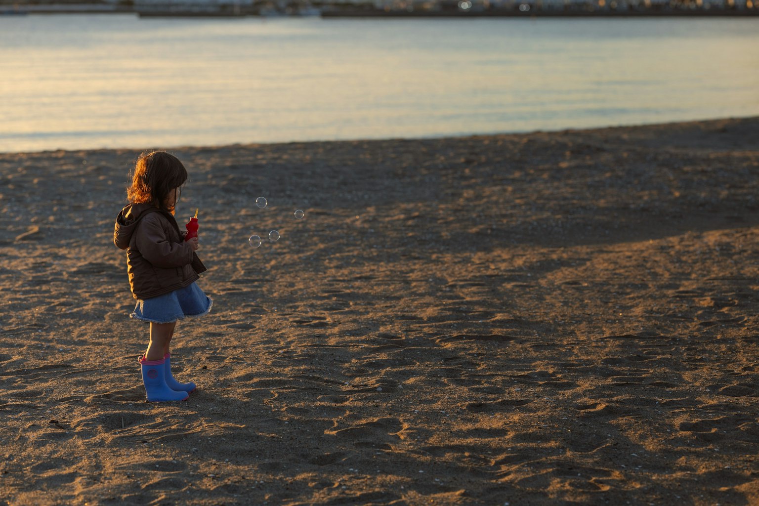 Silhouette eines Kindes, das am Strand spielt, mit dem Meer, das den Sonnenuntergang im Hintergrund reflektiert