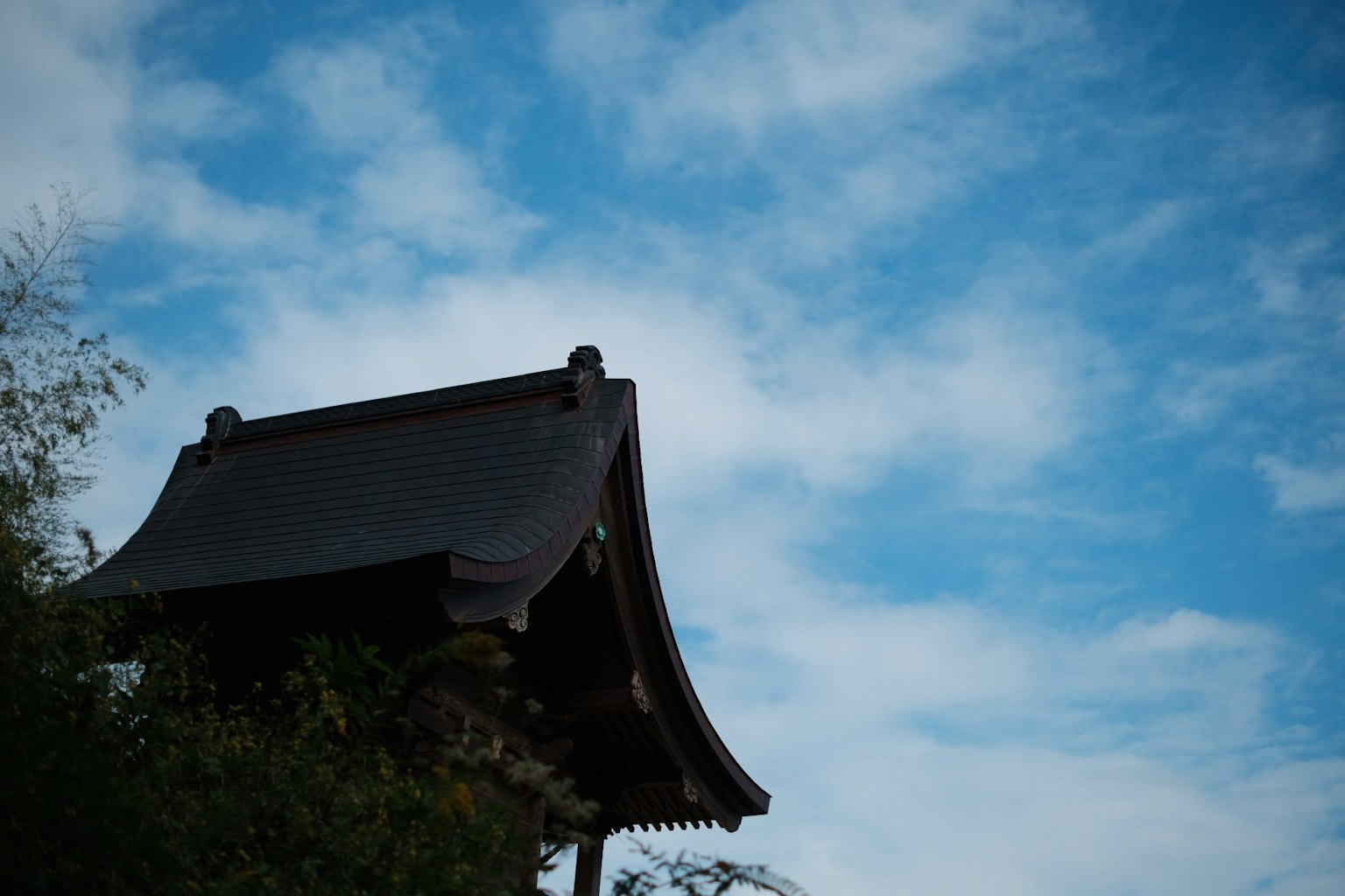 Traditional Japanese building roof under blue sky with clouds