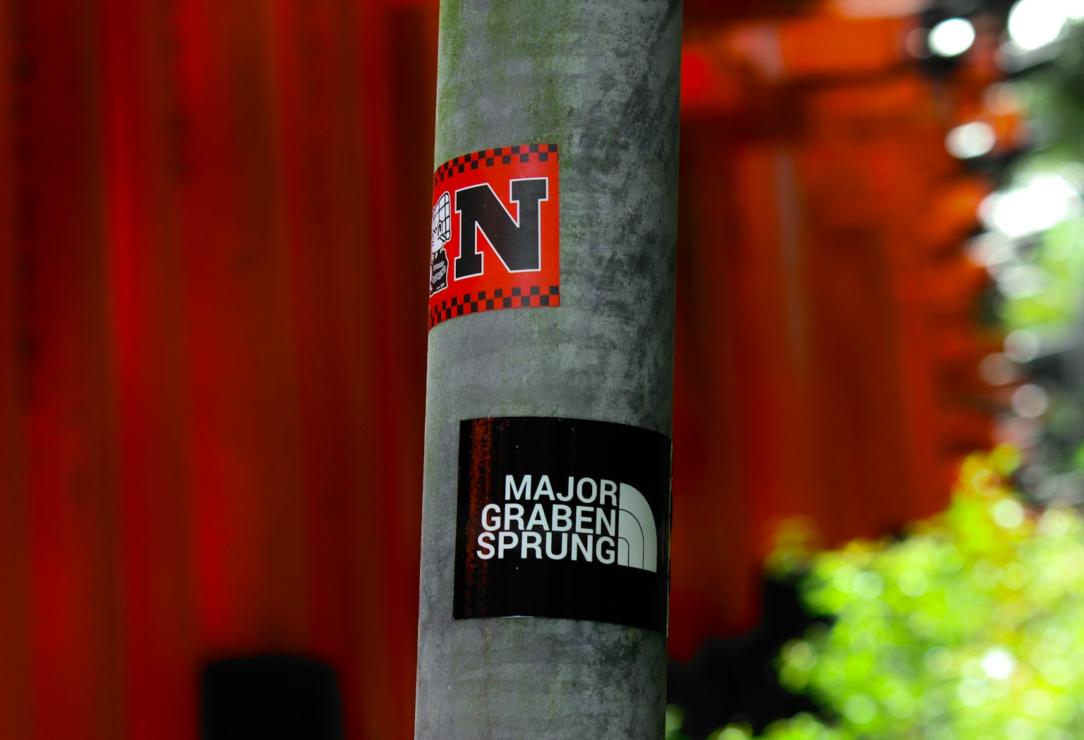 Close-up of stickers on a tree pole featuring a red N logo and black MAJOR GRABEN SPRUNGE text