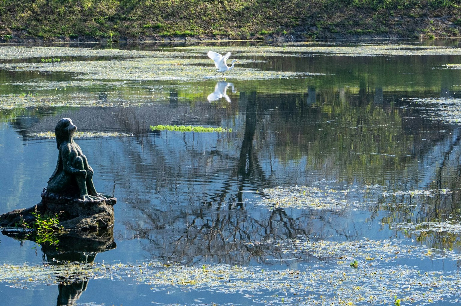 Un paesaggio sereno con una statua vicino allo stagno e un uccello bianco che vola sull'acqua