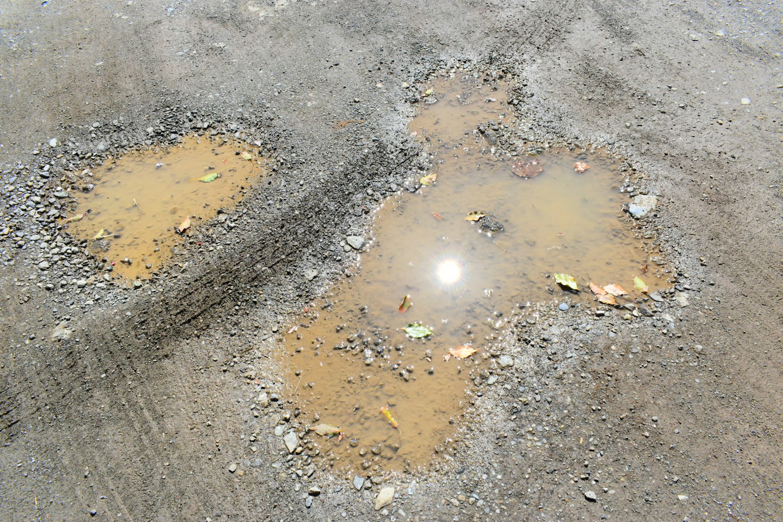 Puddle d'acqua e pietre sparse su una superficie stradale
