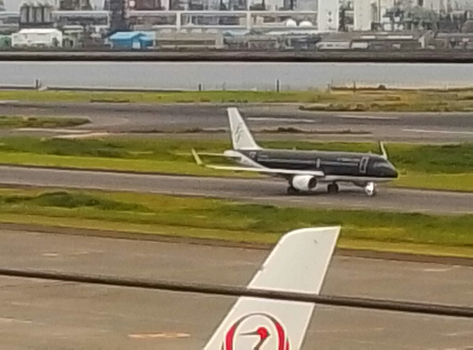 黑色飛機在跑道上滑行，前景是白色飛機的機翼