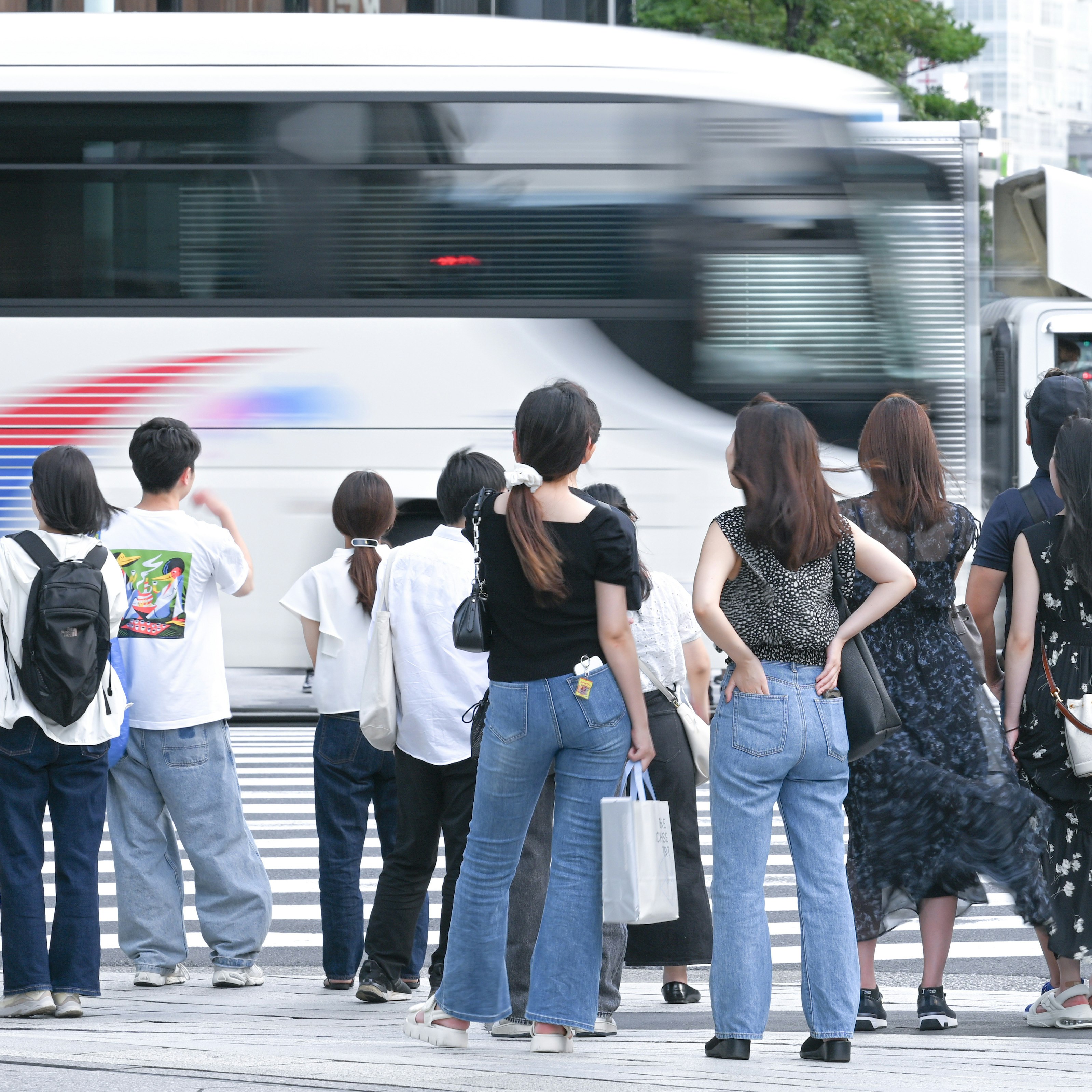 東京の横断歩道で高速バスを待つ人々の後ろ姿