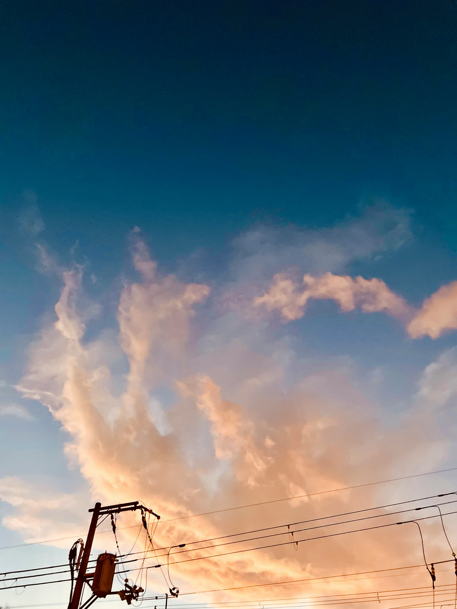 Nubes naranjas contra un cielo azul con siluetas de líneas eléctricas