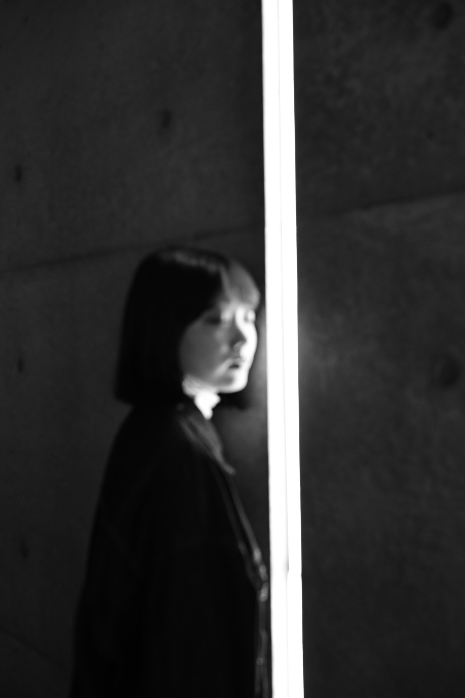 Une femme se tenant devant un fond sombre illuminée par un faisceau de lumière en noir et blanc