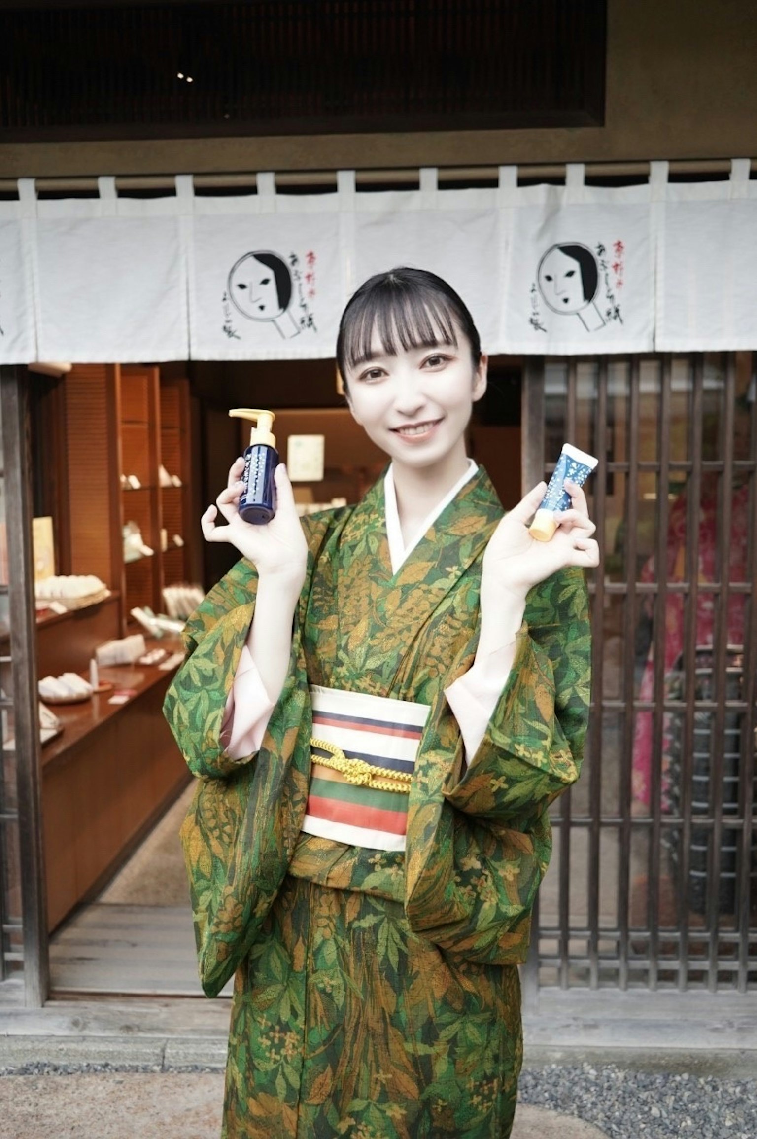 Une femme en kimono vert tient deux petits objets en souriant