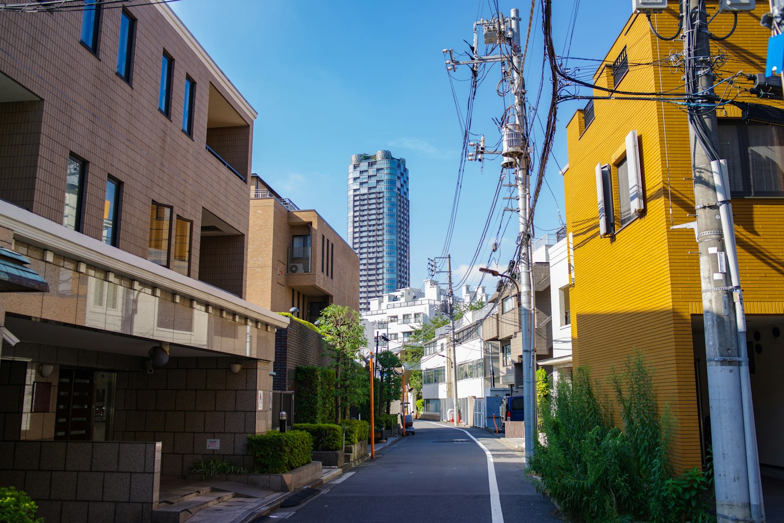 Narrow street lined with residential buildings and a skyscraper under blue sky