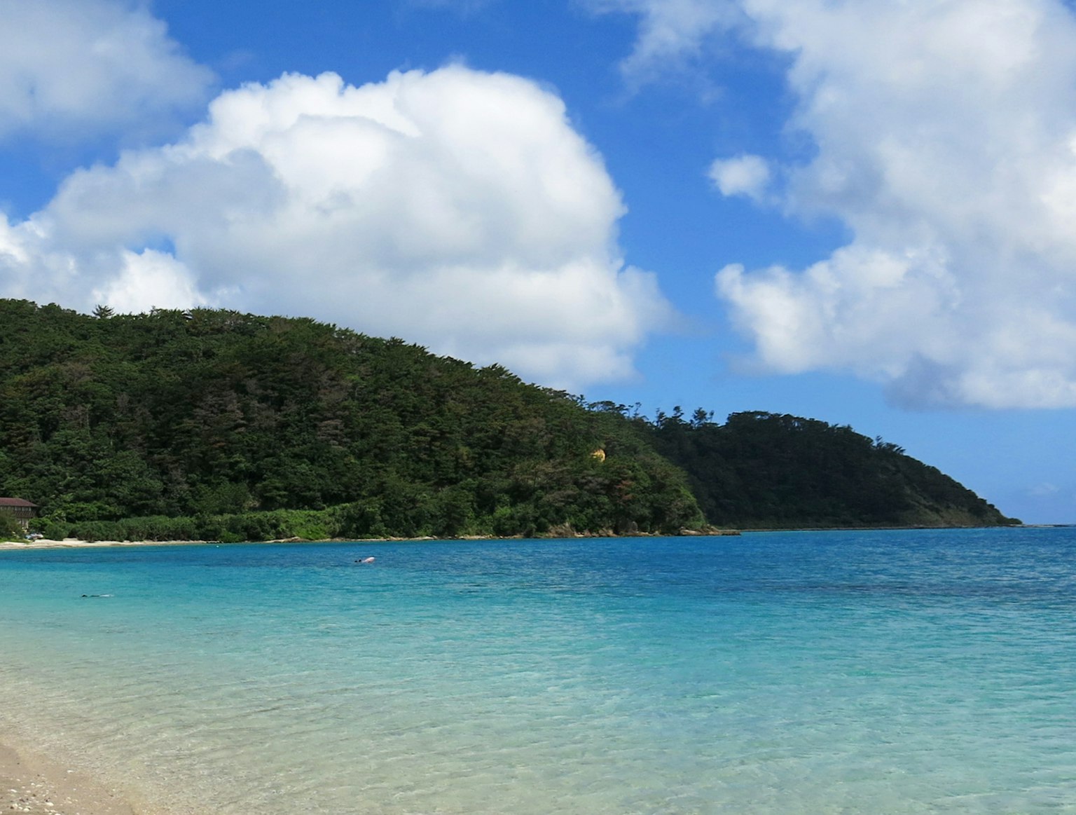 海滩的风景 蓝色水域和白色沙滩 绿色山丘在蓝天之下