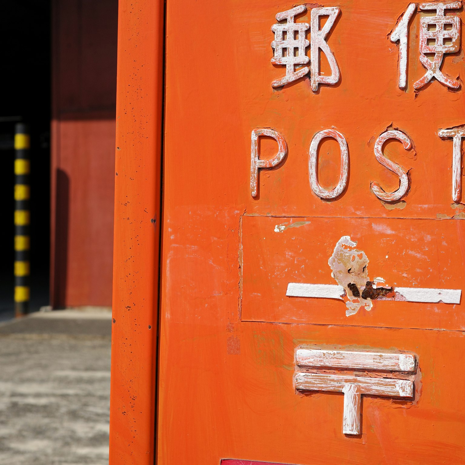 Close-up shot of an orange mailbox featuring English and Japanese lettering
