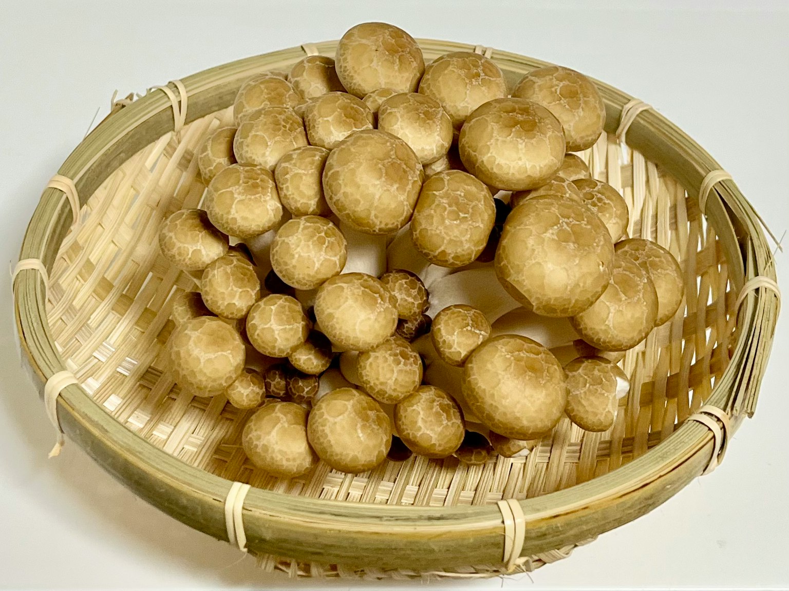 A large cluster of brown mushrooms arranged in a woven bamboo basket
