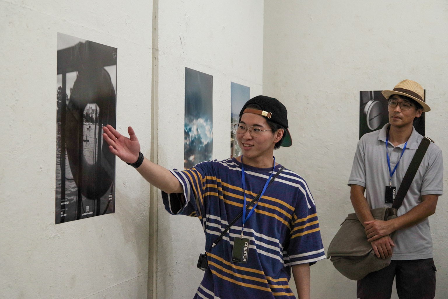 A man gesturing towards a photo at an exhibition with another person observing