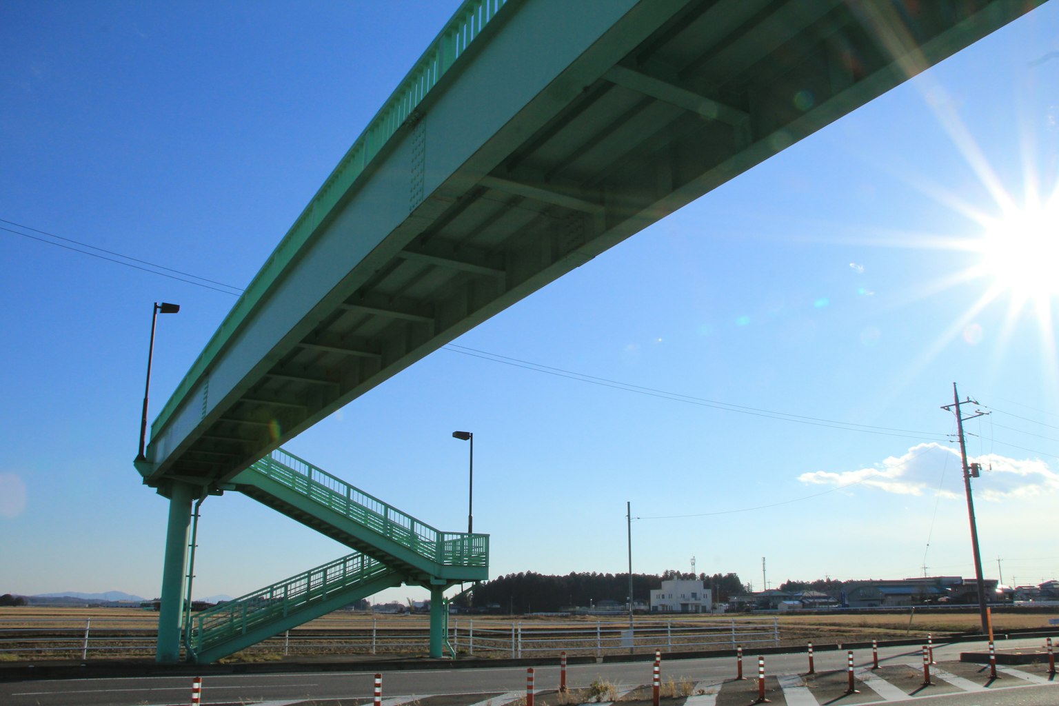 Un ponte pedonale verde con scale sotto un cielo azzurro