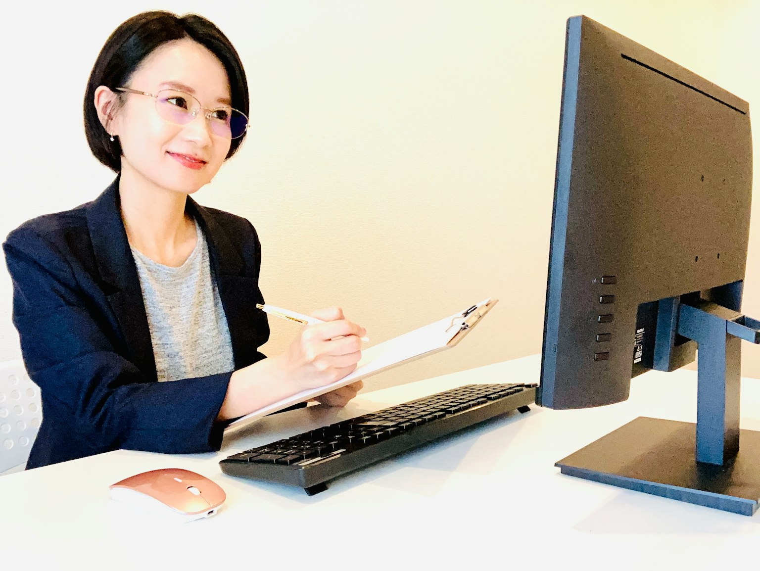 Seorang wanita tersenyum saat mencatat di depan komputer di kantor