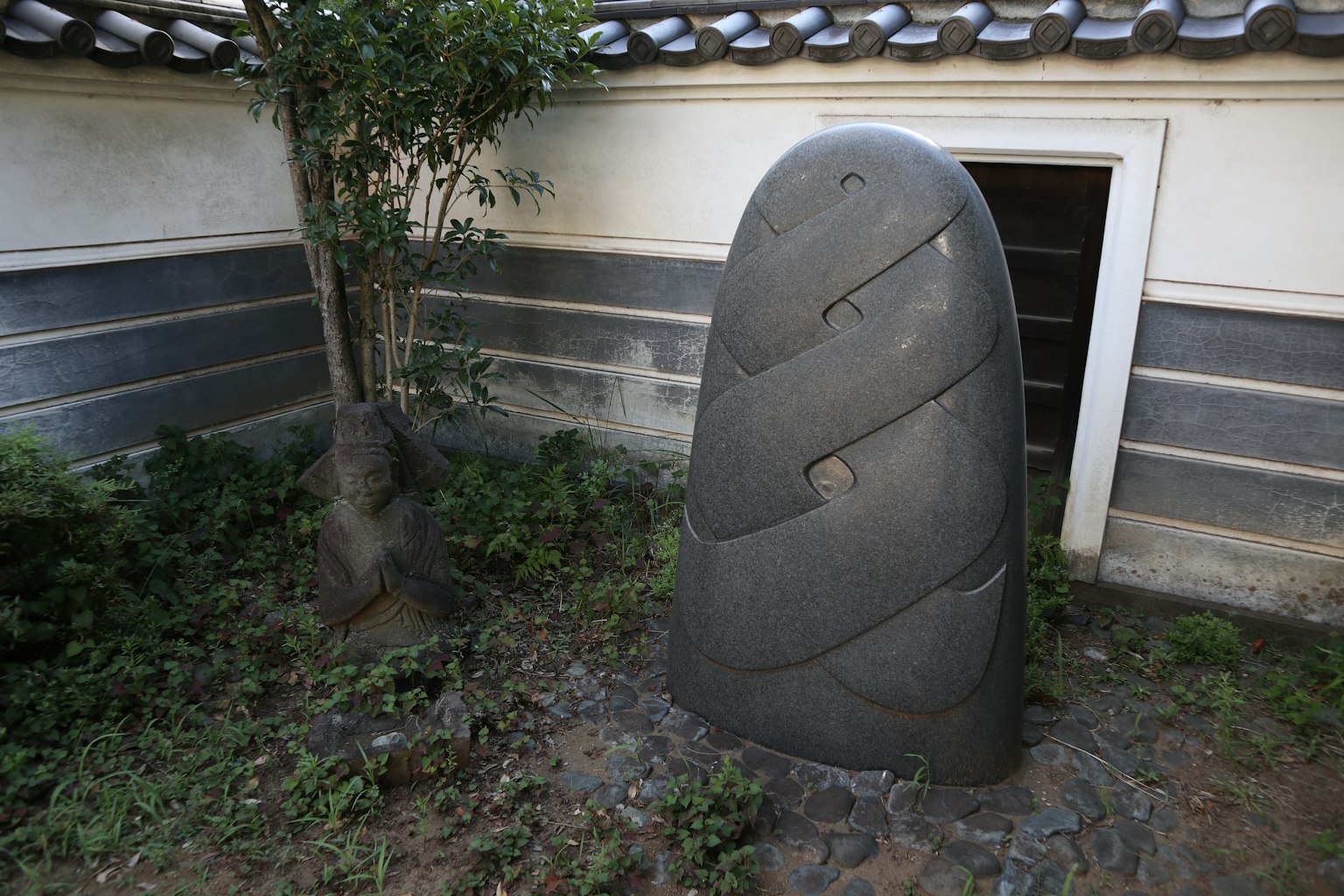 Glatte schwarze Steinskulptur in einem Garten mit umliegendem Grün