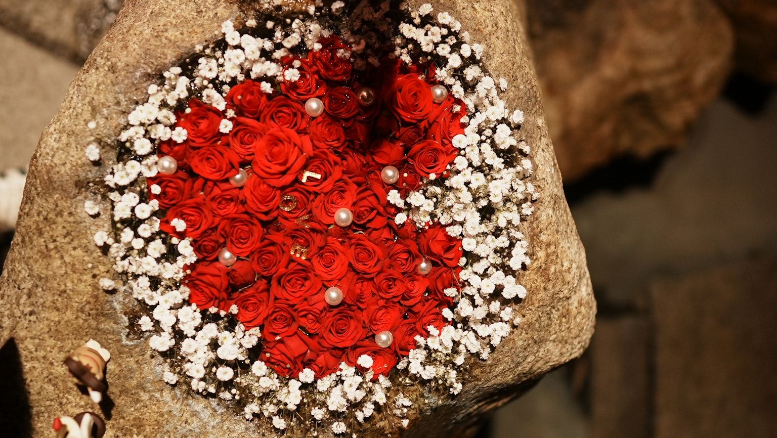 Arreglo de rosas rojas y flores blancas sobre una superficie de piedra