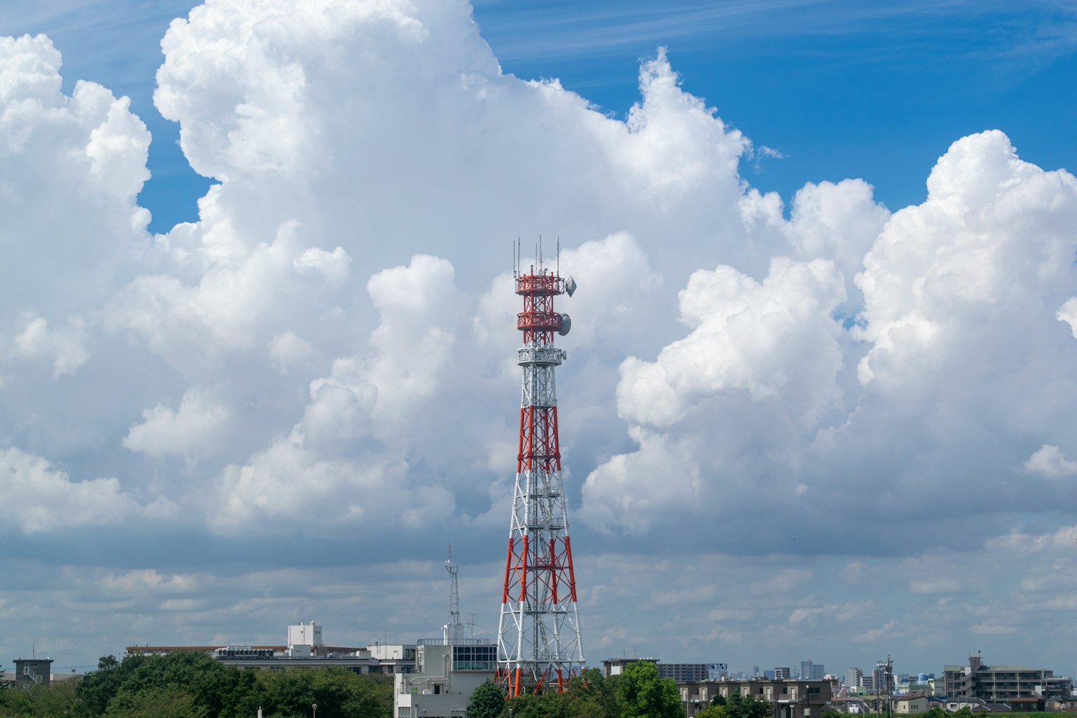 Menara komunikasi menjulang di bawah langit biru dengan awan putih