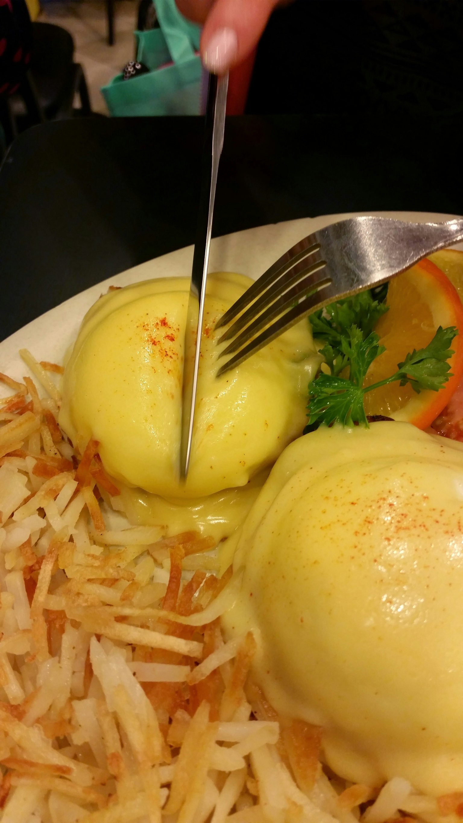 Una forchetta e un coltello che tagliano uova benedette su un letto di patate hash