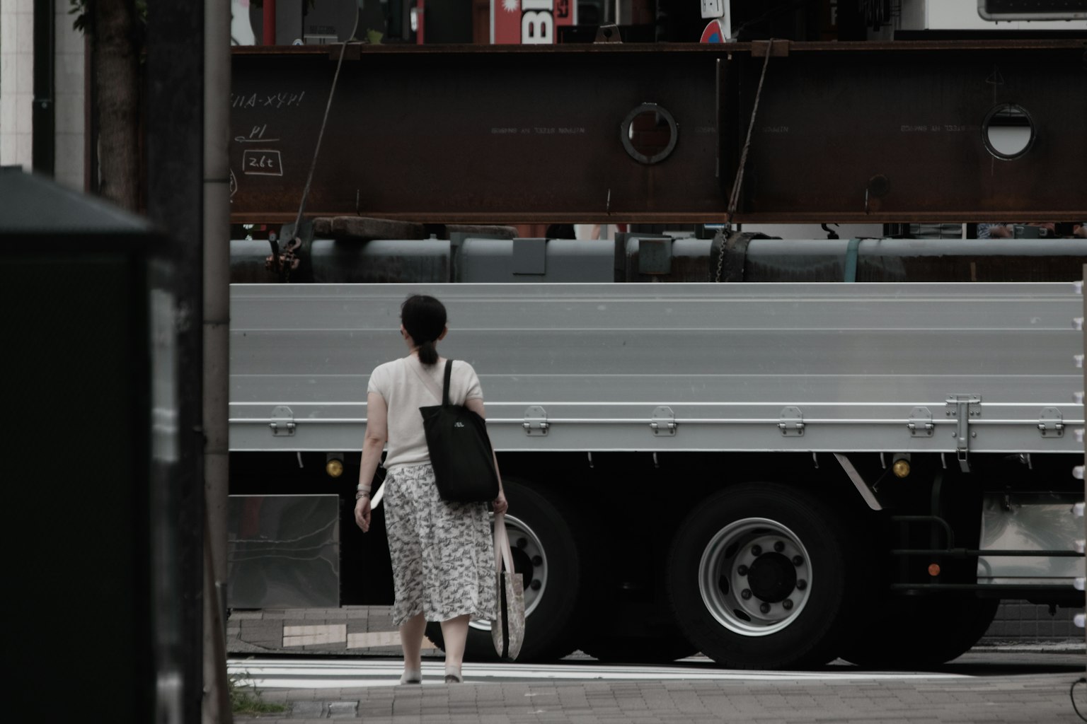 Một người phụ nữ đi bộ trước xe tải mặc váy trắng và cầm túi đen