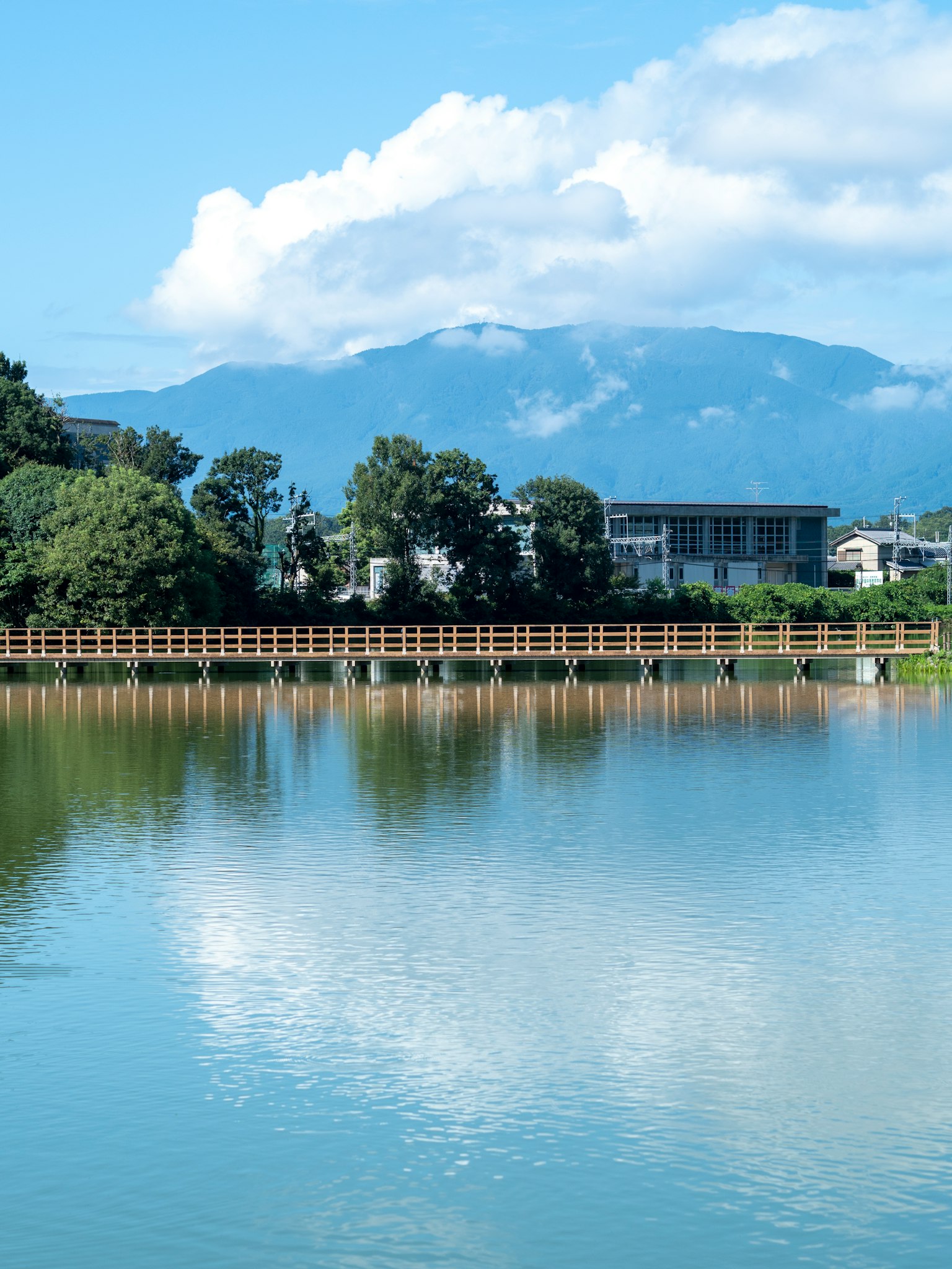 Lago tranquilo reflejando el cielo azul y las nubes blancas con montañas y edificios al fondo