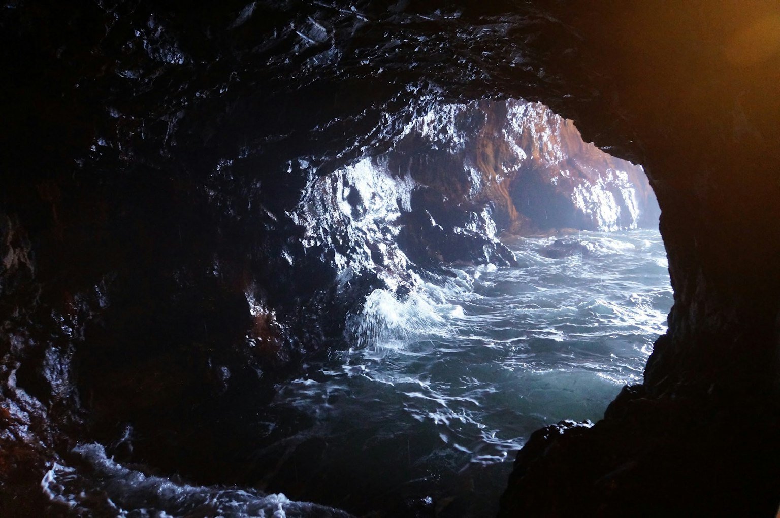 Vista desde el interior de una cueva marina mostrando olas y rocas afuera